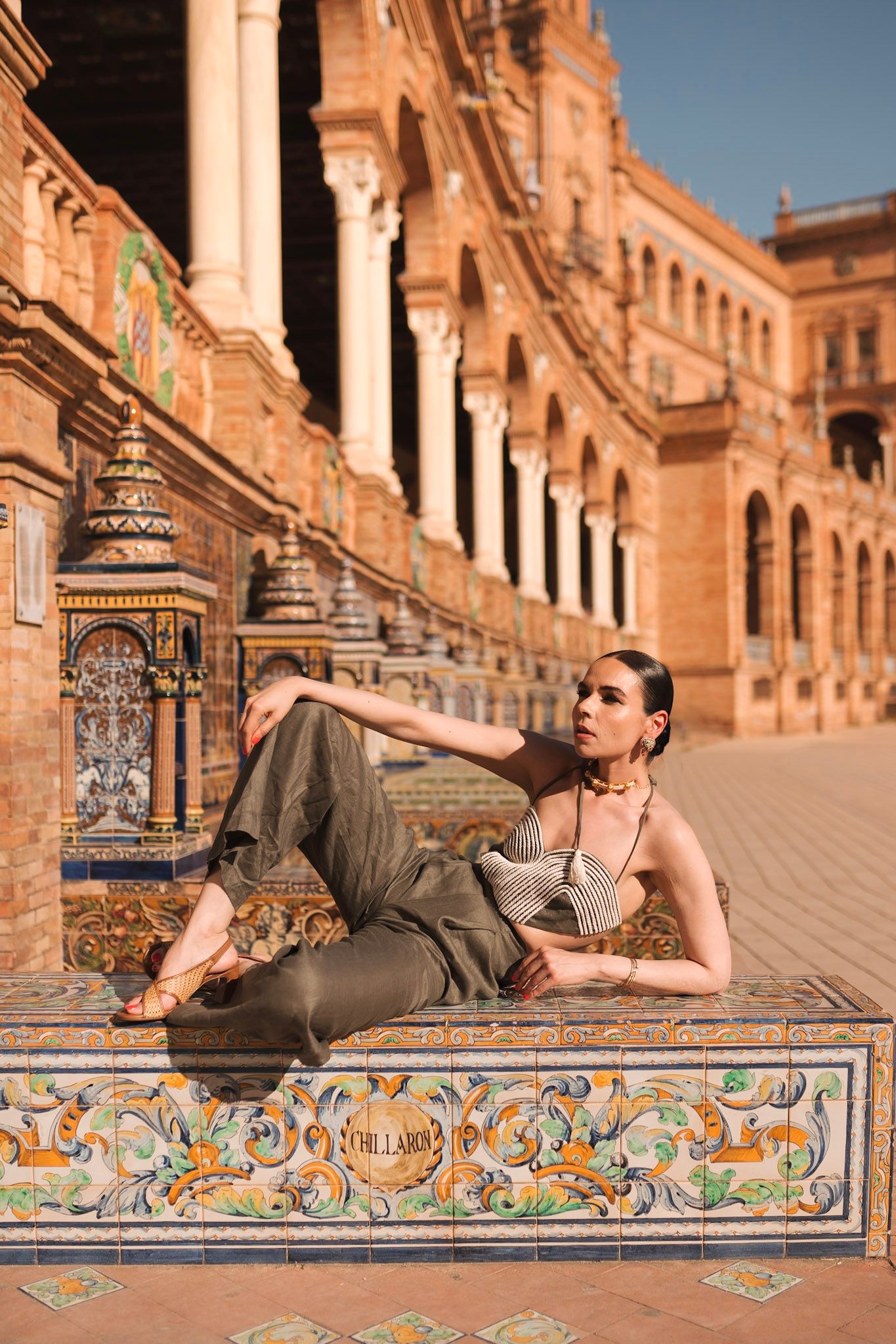 Woman in striped top and olive pants posing on mosaic bench at Plaza de España.