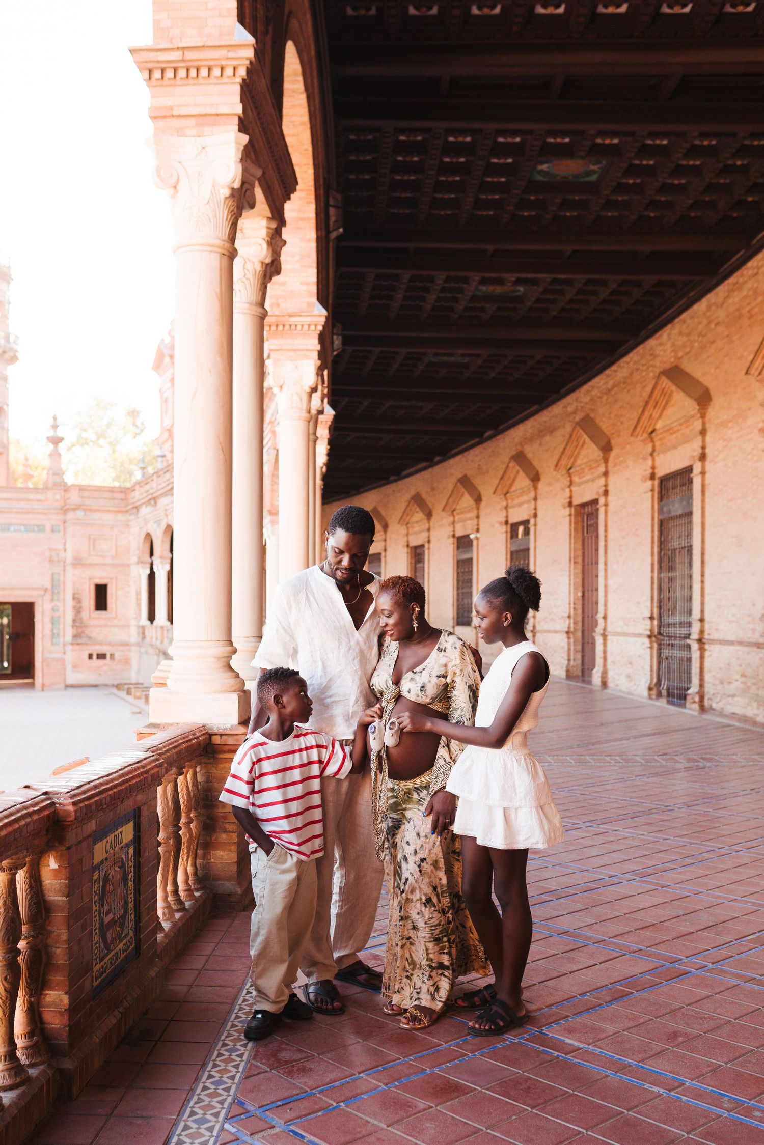 A joyful Black family exploring the ornate arcade of Plaza de España in Seville, Spain.