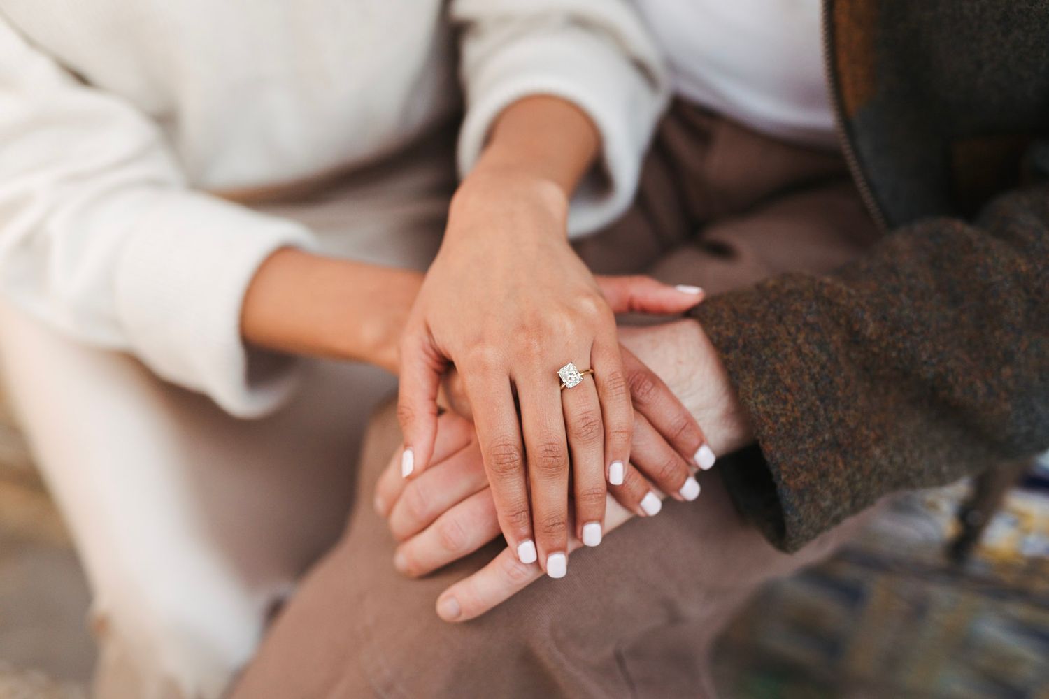 Close-up of a woman's hand displaying a stunning diamond engagement ring with white manicured nails.