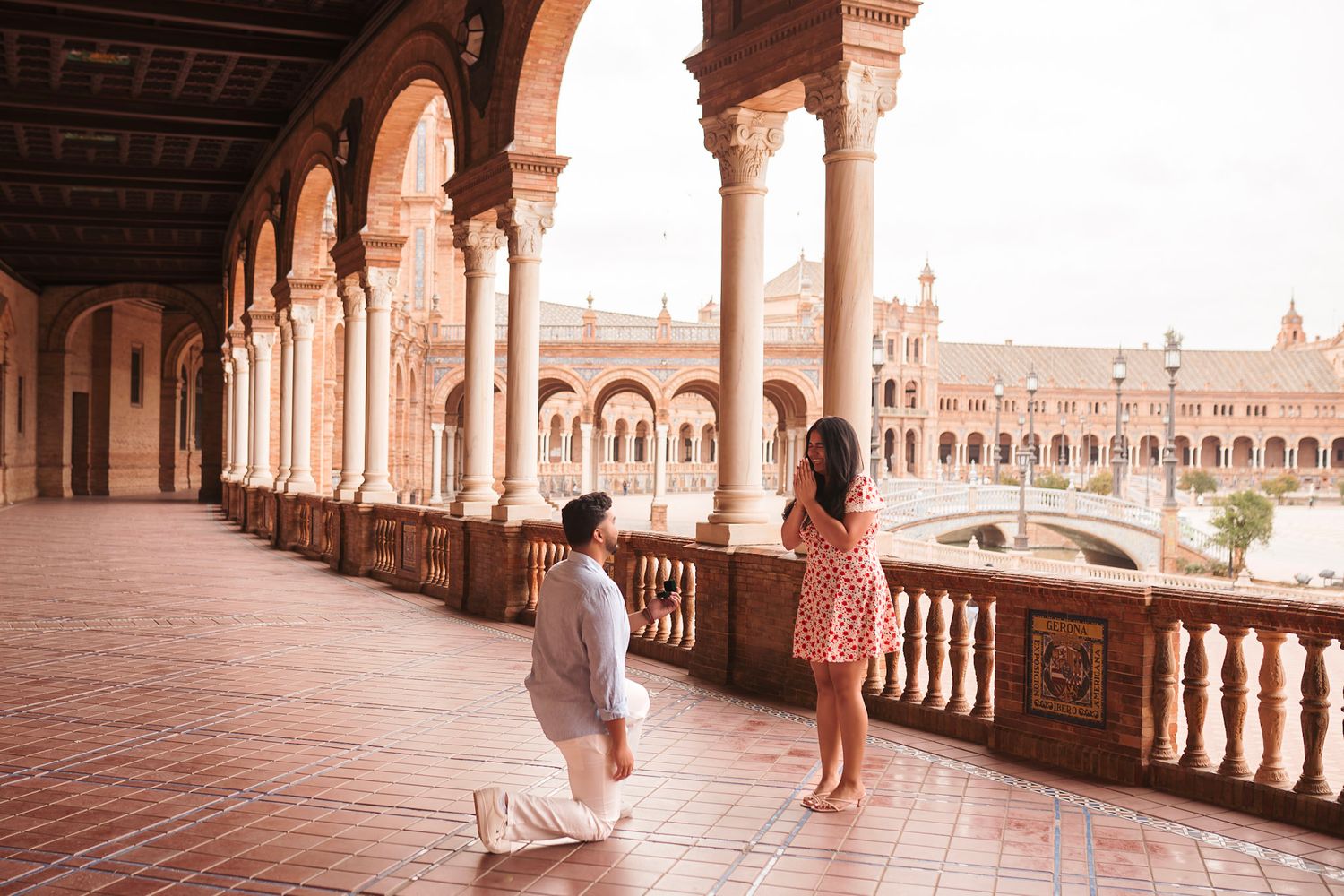 Man proposing on one knee to woman at the stunning colonnade of Plaza de España, Seville.
