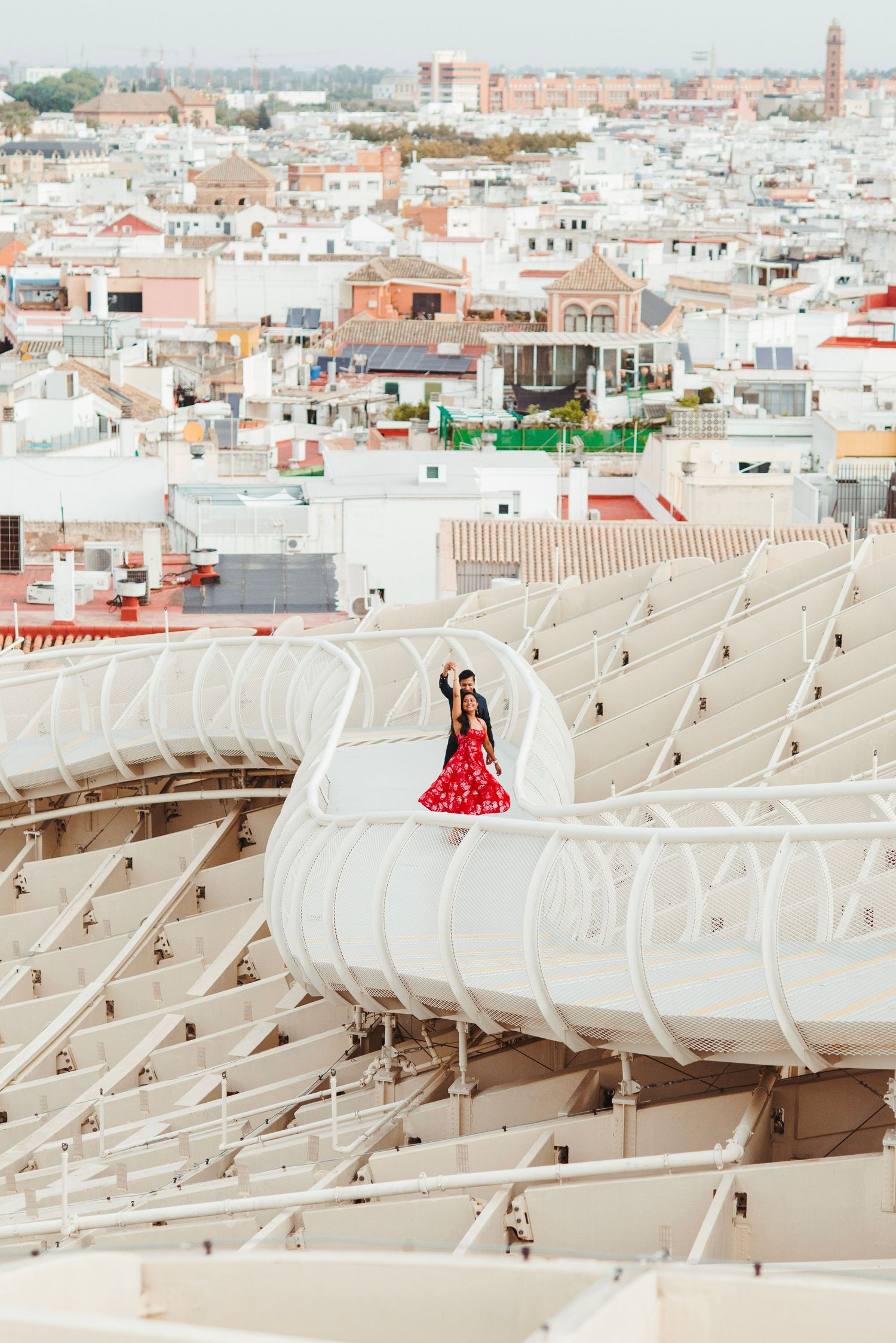 Woman in red flamenco dress posing atop Metropol Parasol with Seville cityscape behind.
