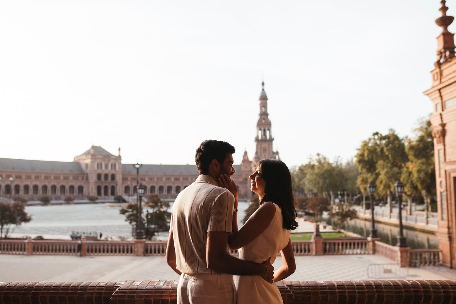 Romantic couple embracing on a balcony overlooking Plaza de España in Seville, Spain.