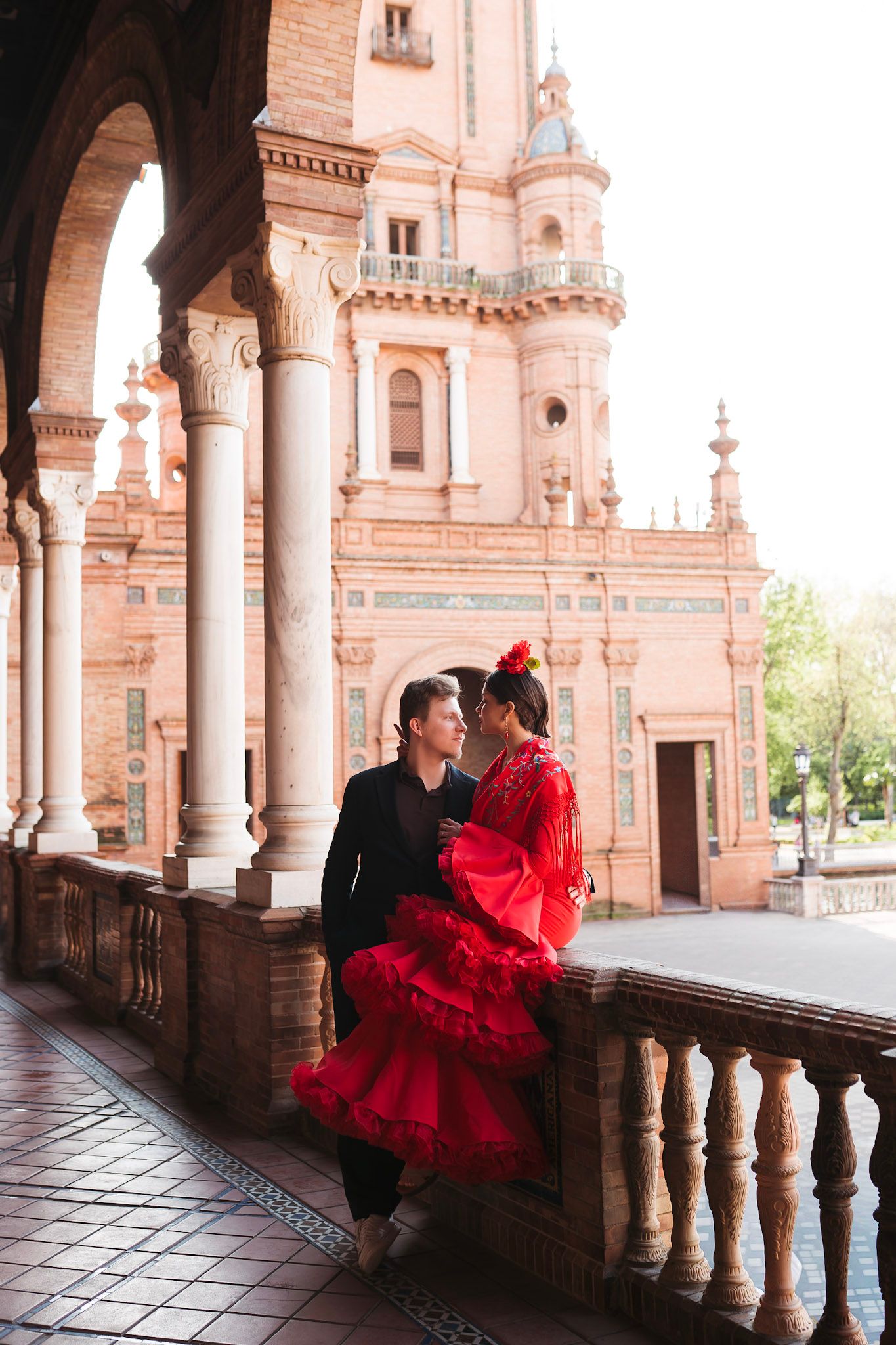 Romantic flamenco couple embracing on balcony at Plaza de España, woman in red ruffled dress, Seville.