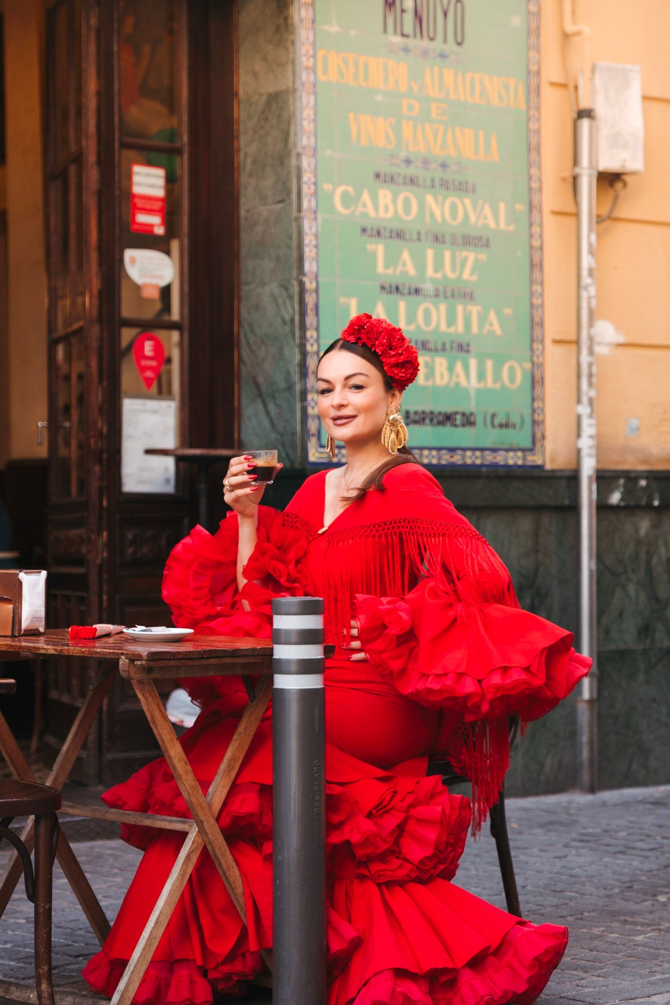 Woman in red flamenco dress sitting at outdoor cafe table in Seville, Spain.