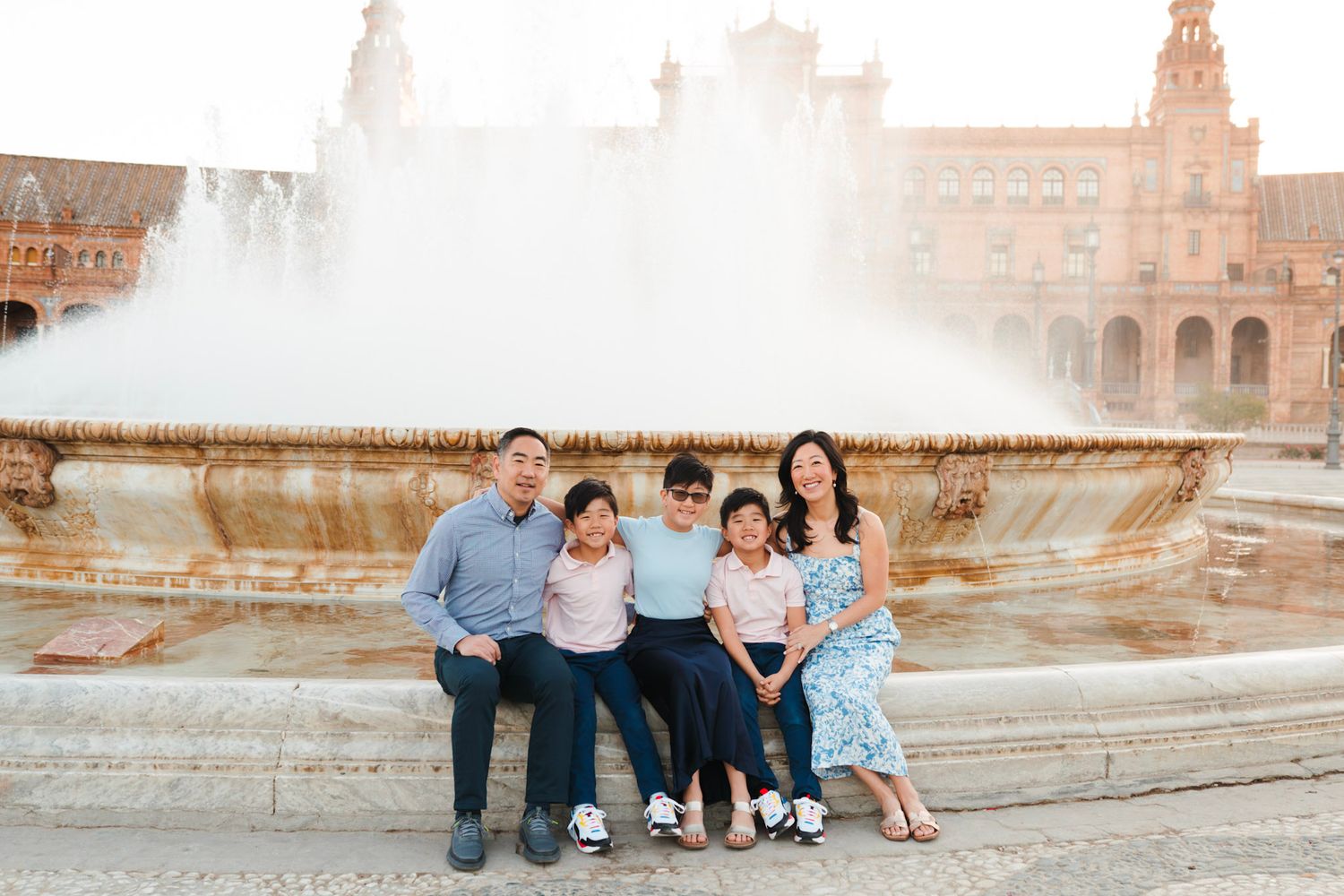 A family of five sitting together in front of a fountain at Plaza de Espana in Seville, Spain.