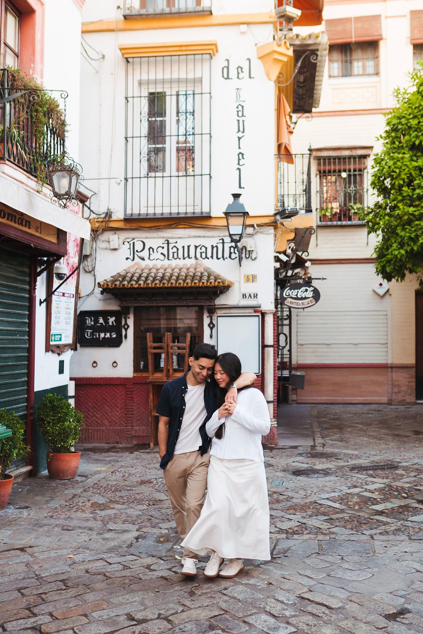 Couple walking together on cobblestone streets near a traditional restaurant in Seville.