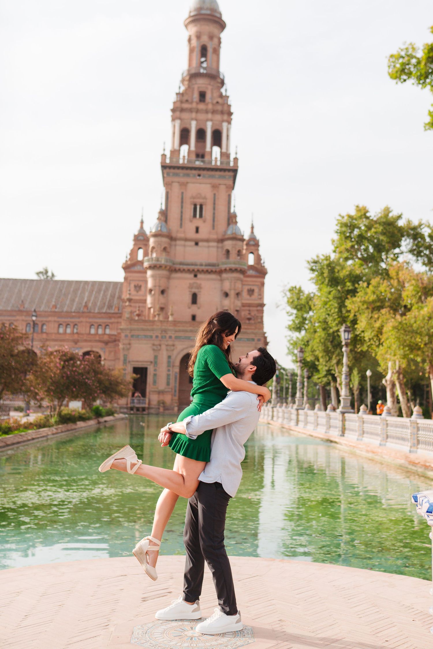 Couple embracing romantically in front of Plaza de España tower and canal in Seville, Spain.