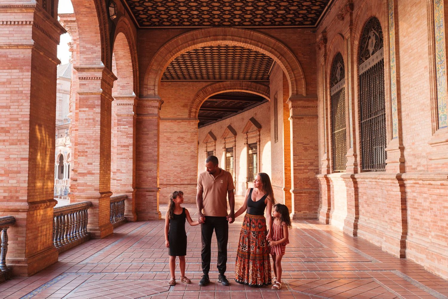 Family of four exploring ornate brick archways at Plaza de España, Seville, Spain.