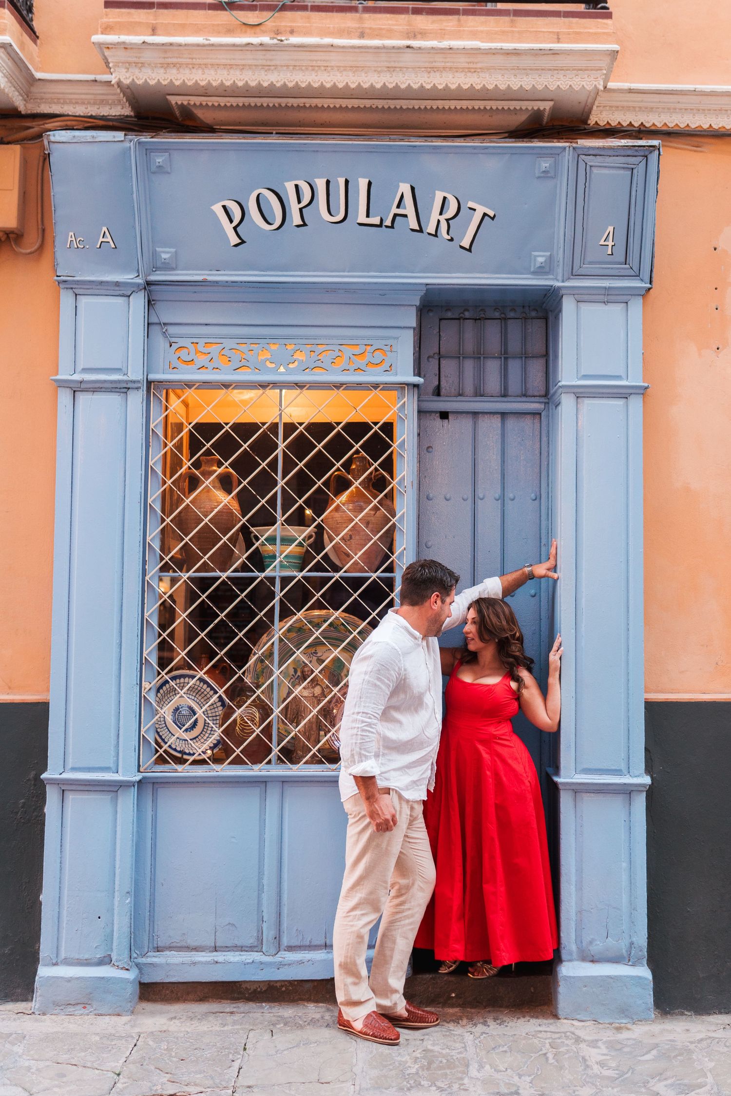 Couple posing in front of a blue-framed Populart shop entrance, woman in red dress, man in white shirt, Seville Spain.