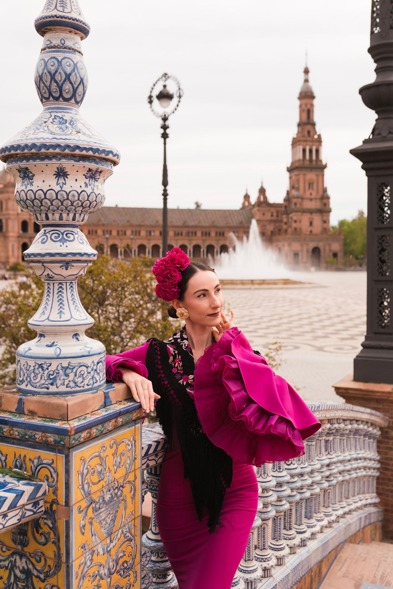 Flamenco dancer in magenta dress with black shawl leaning on decorative tiled railing at Plaza de España.