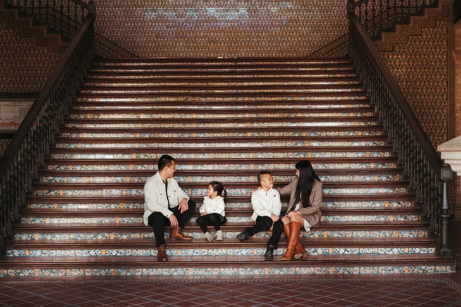 Family of four sits and interacts on the iconic tiled staircase of Plaza de España in Seville.