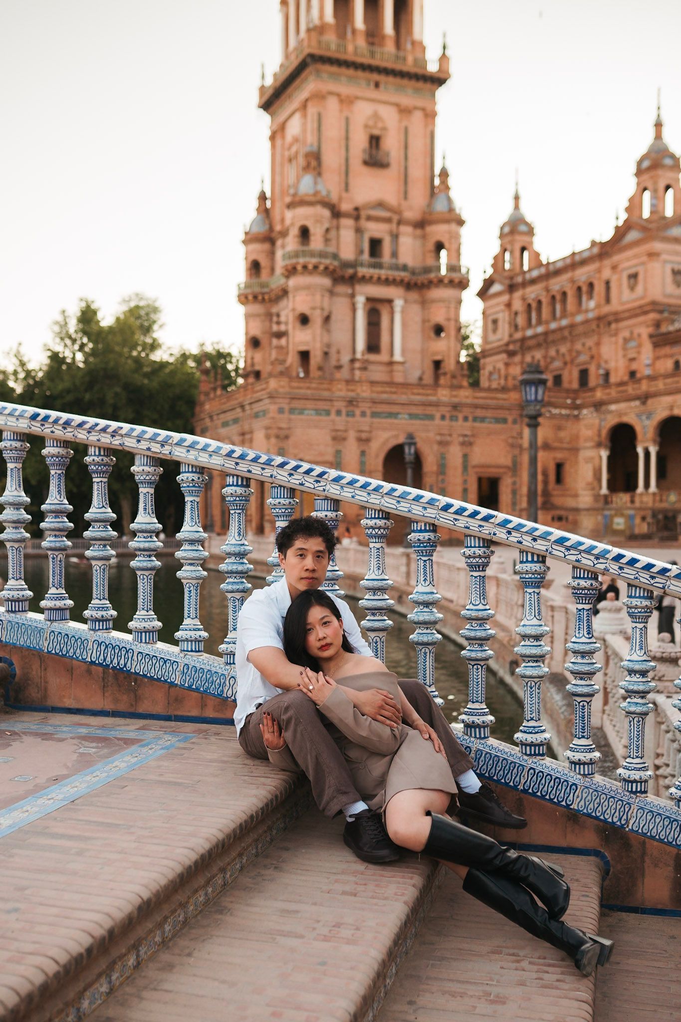 Couple sitting together on ornate tiled steps at Plaza de Espana, Seville, Spain.