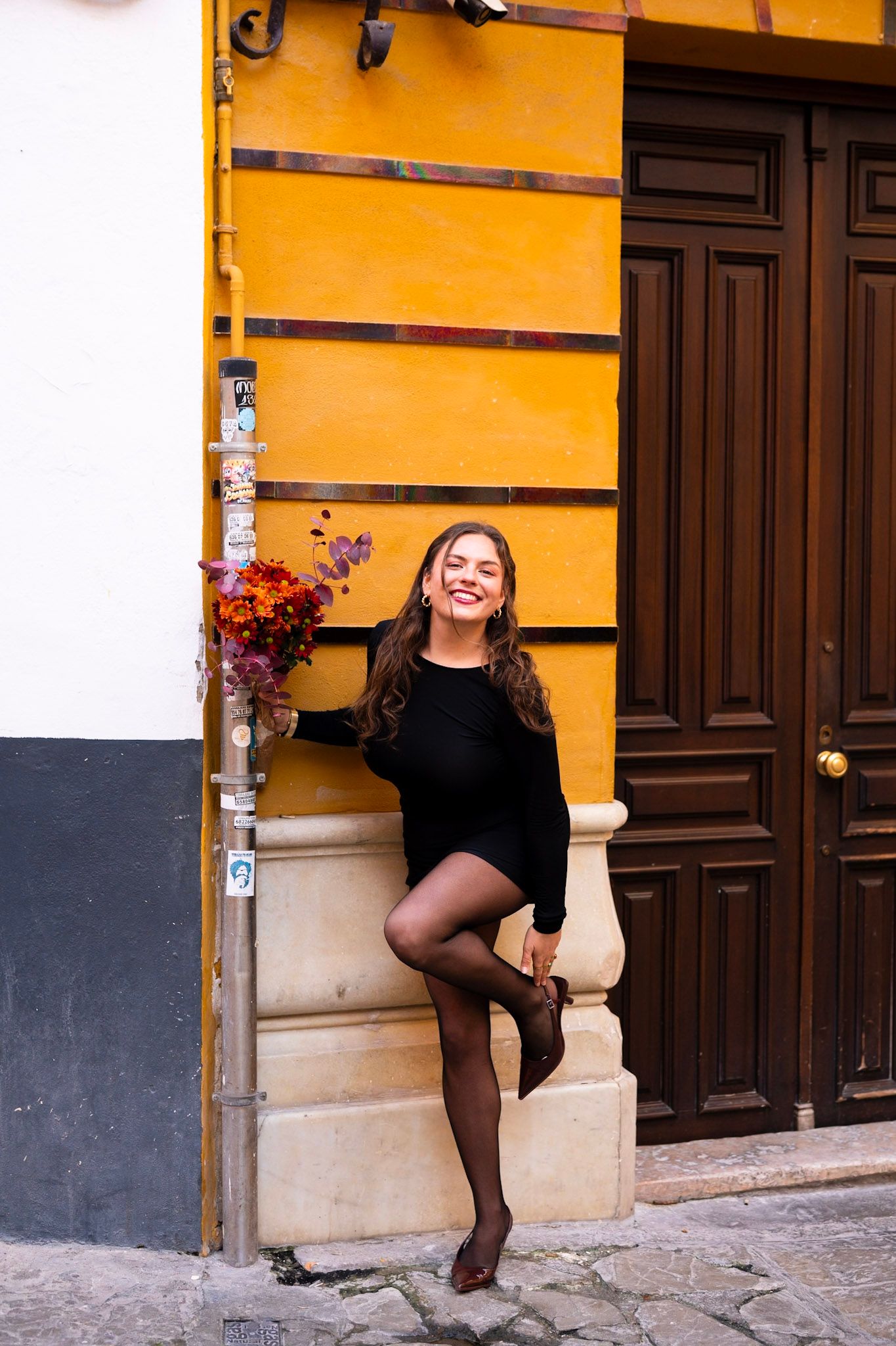Smiling woman reads Diario de Sevilla newspaper on bench surrounded by orange flowers in sunny plaza.