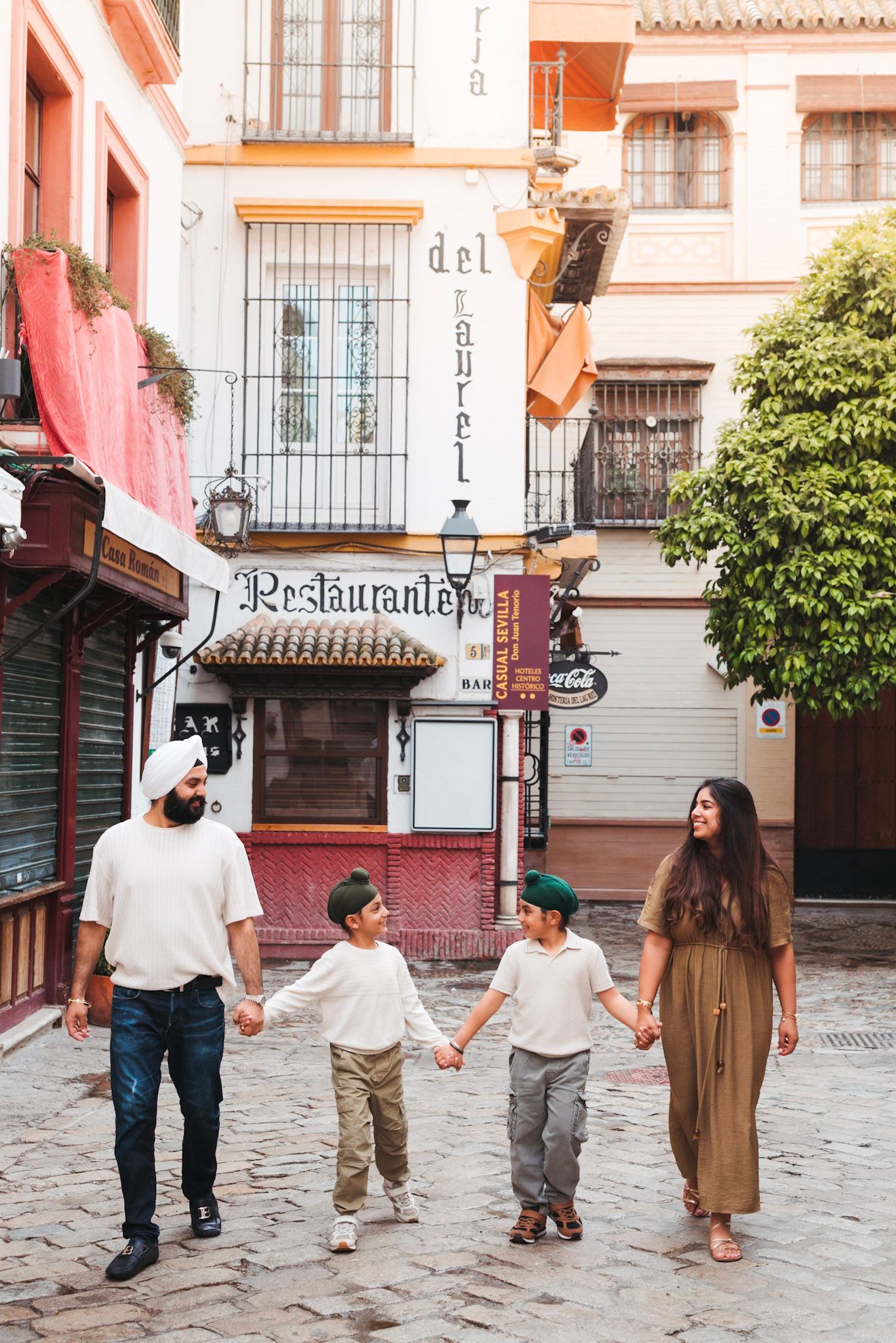 Family of four holding hands while walking cobblestone streets near a restaurant in Seville.
