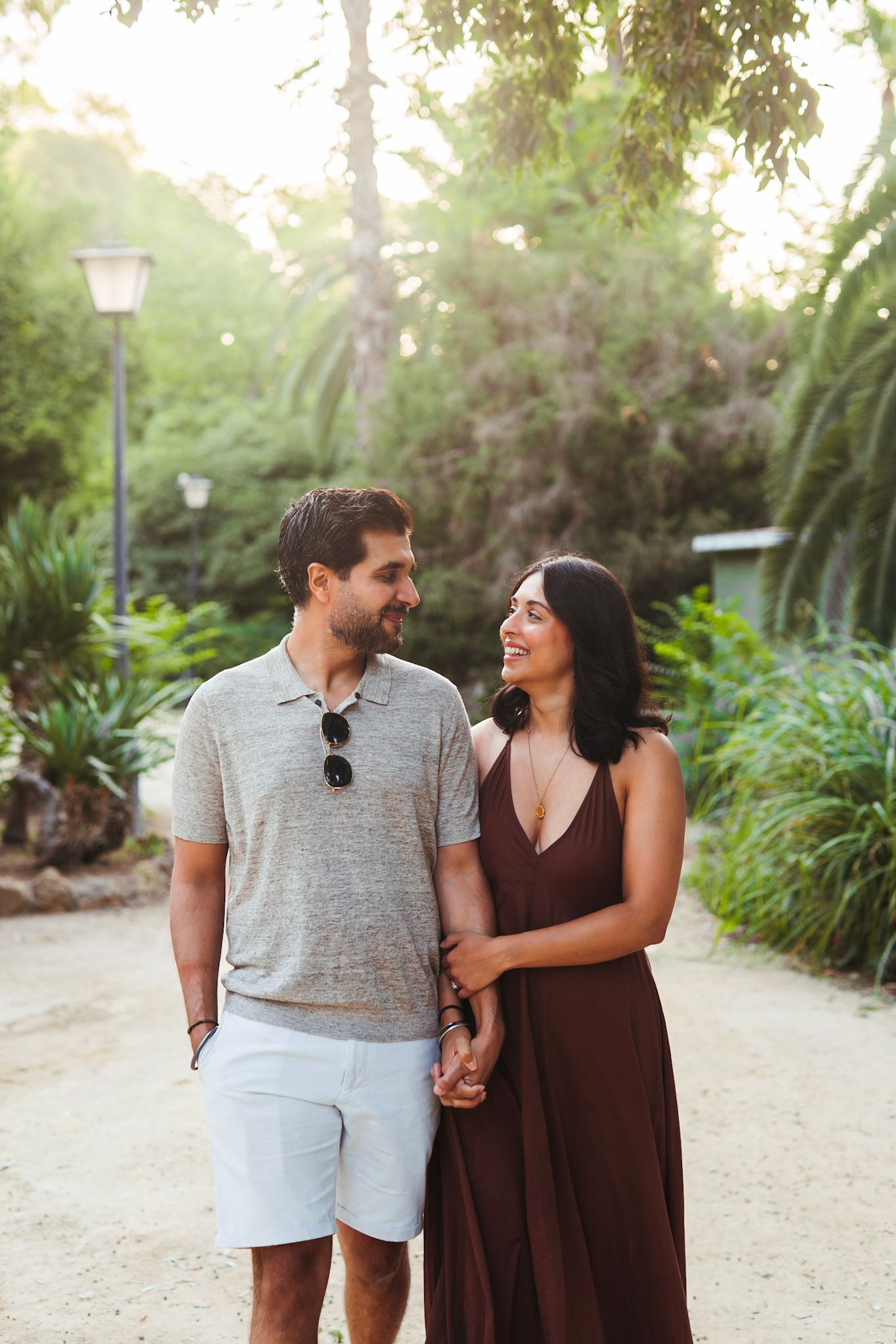 Happy couple walks hand in hand through lush tropical garden path at golden hour.