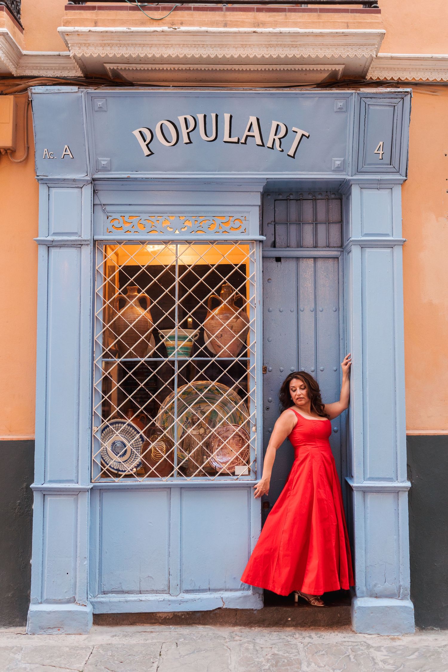 Woman in red dress posing elegantly at the entrance of Populart shop with blue facade.