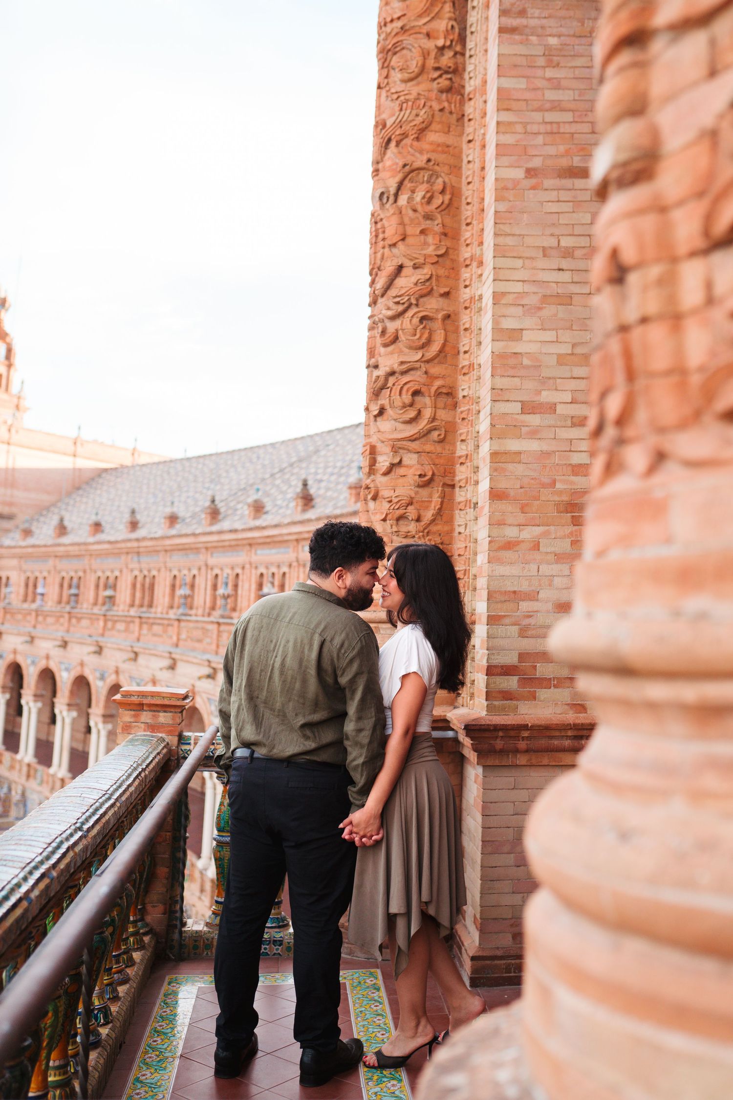 Couple sharing a romantic moment on a balcony at Plaza de España, Seville, surrounded by ornate brick architecture.