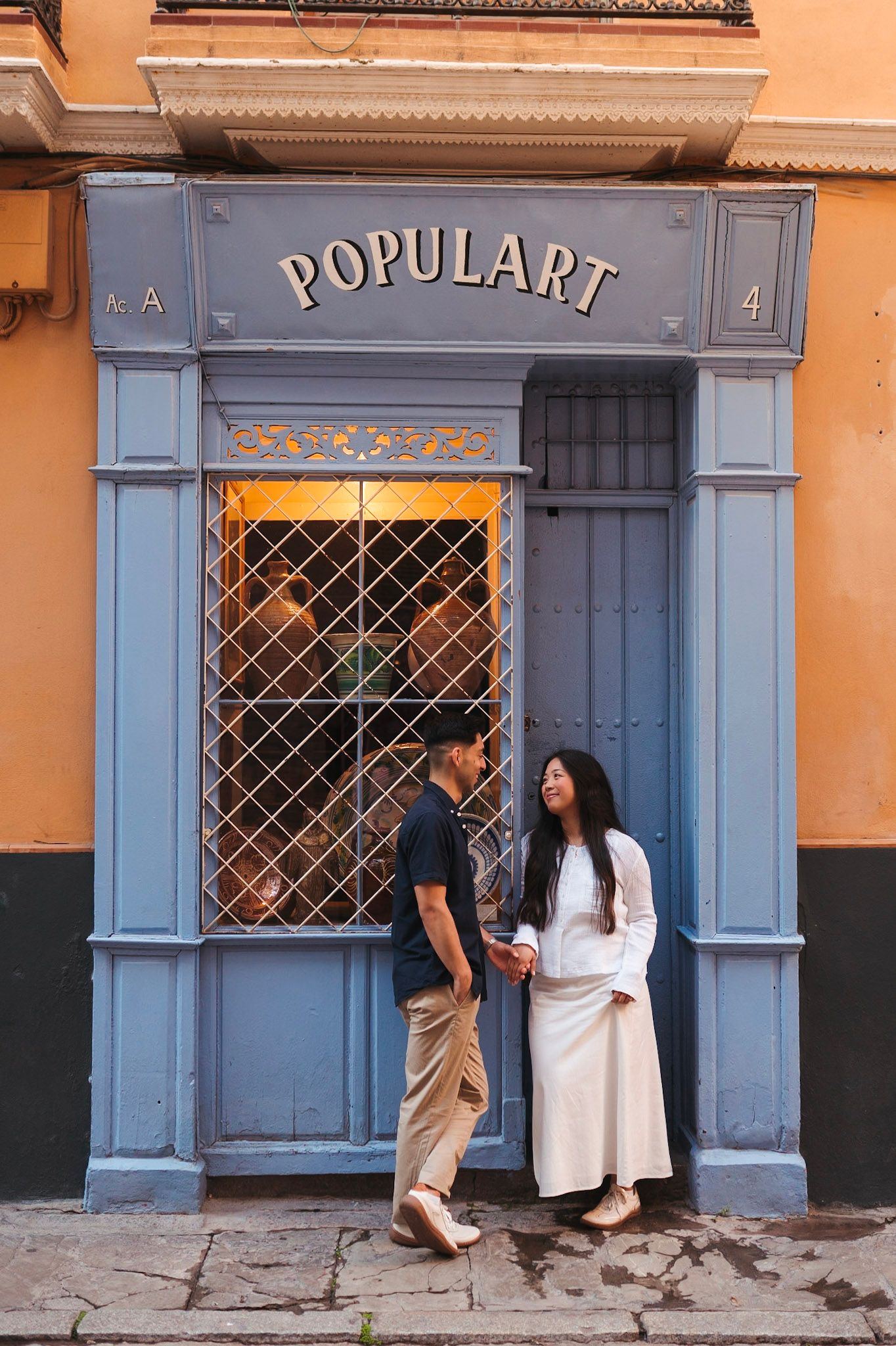 Couple standing together outside a blue-framed Populart shop on a charming city street.