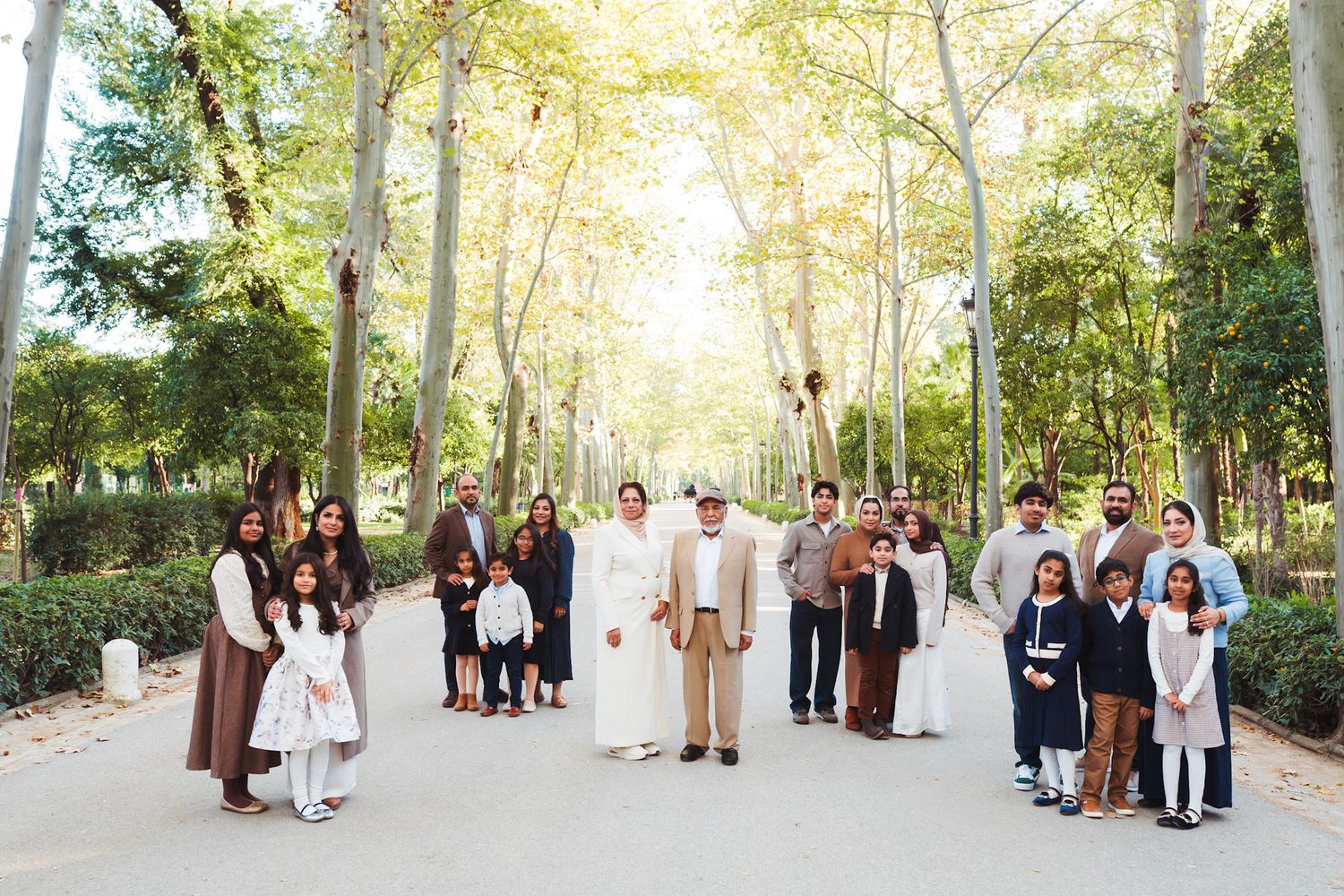 A large multigenerational family posing together on a tree-lined path in a sunny park in Seville, Spain.