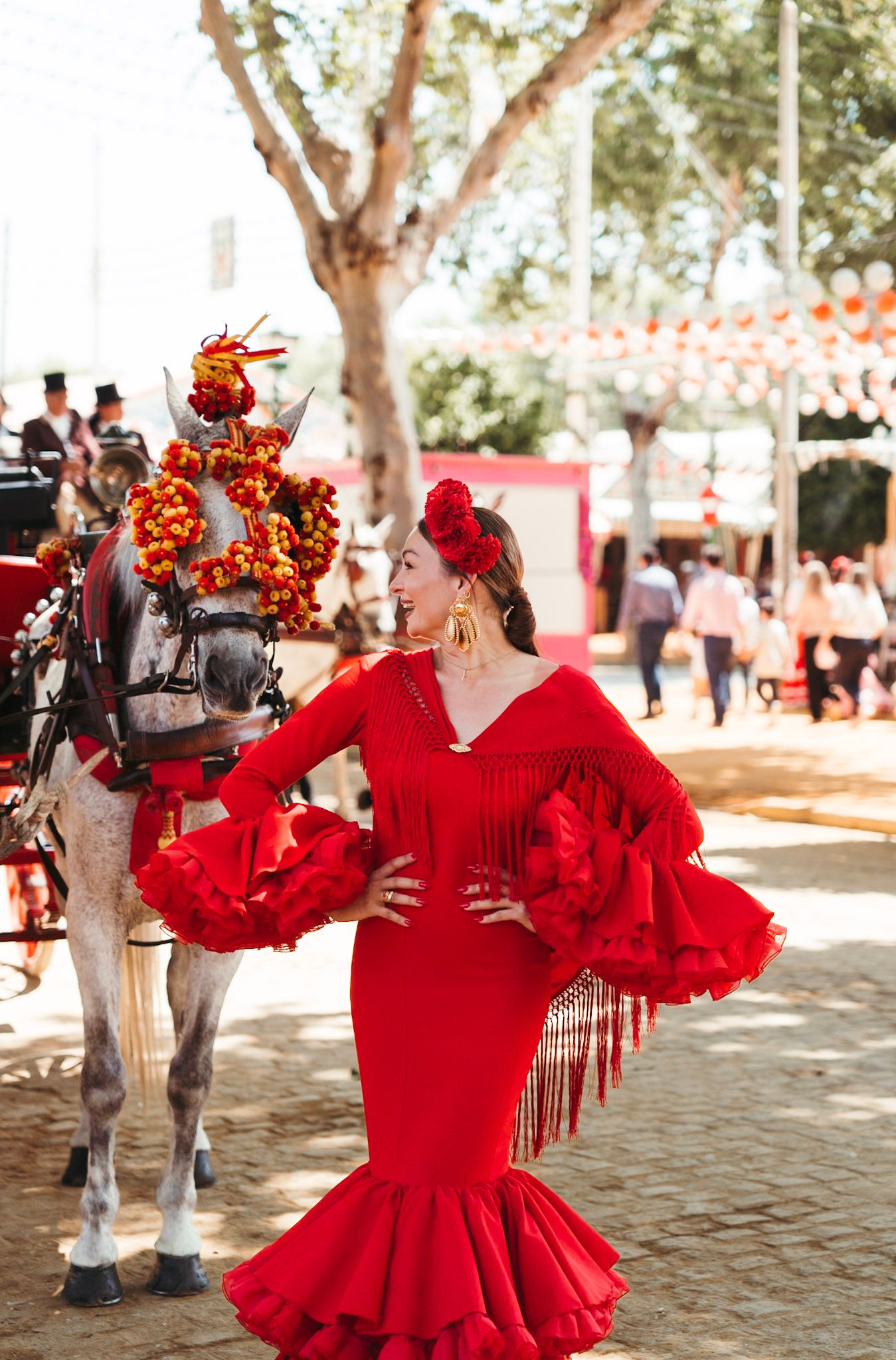 Flamenco dancer in red dress stands beside decorated horse at Seville April Fair.