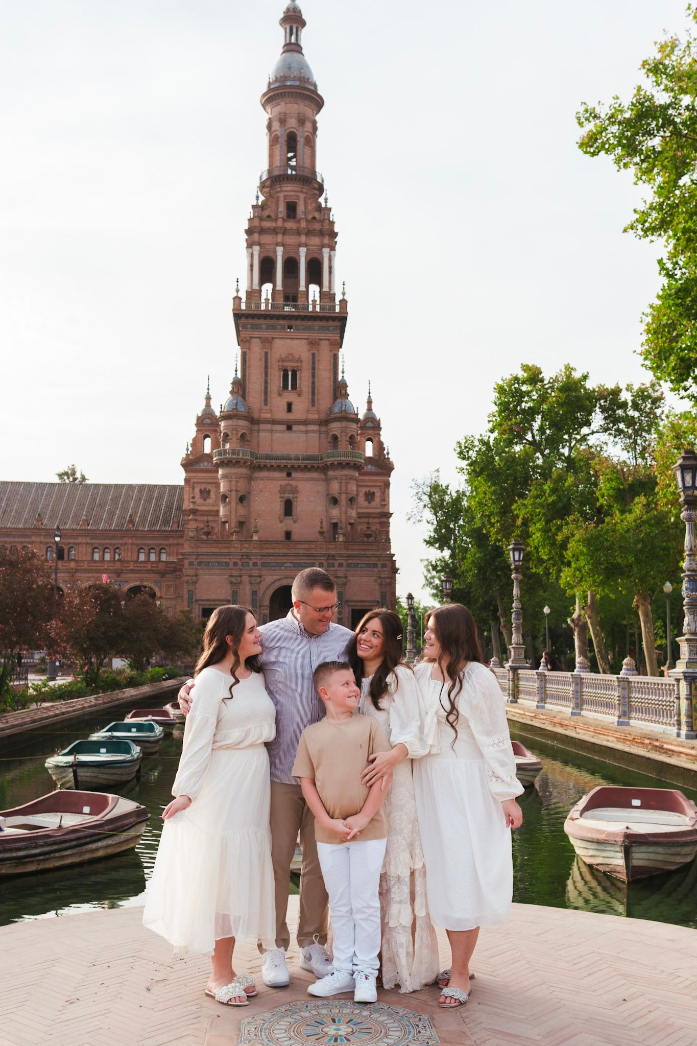 Family of five in white outfits gathered near canal at Plaza de España, Seville.