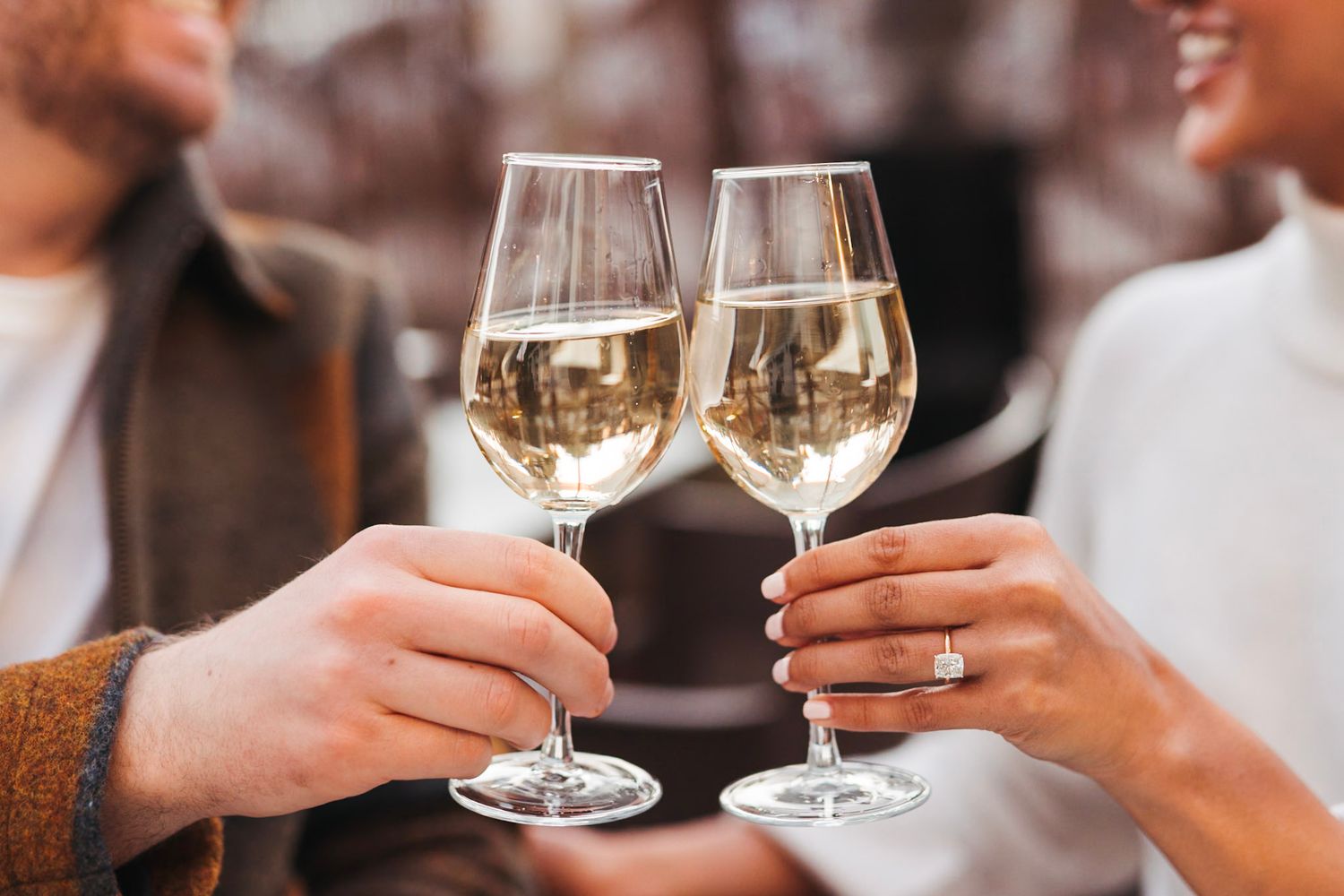 Couple celebrating with a toast of white wine glasses at a romantic restaurant setting.