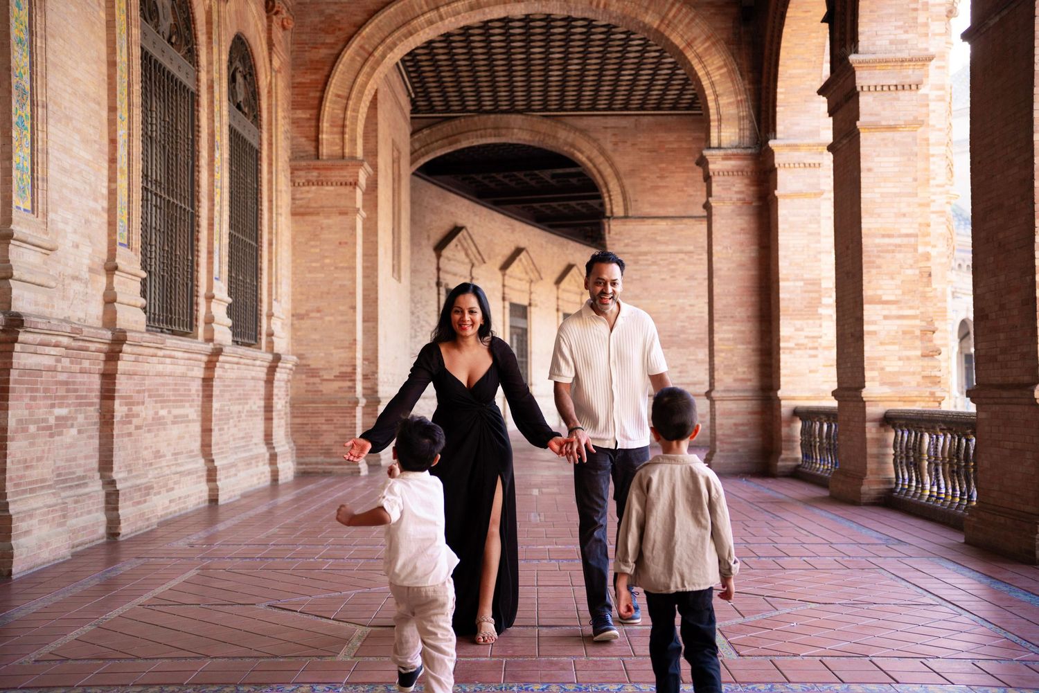 Family walks hand in hand through ornate arched corridors of Plaza de España in Seville, Spain.