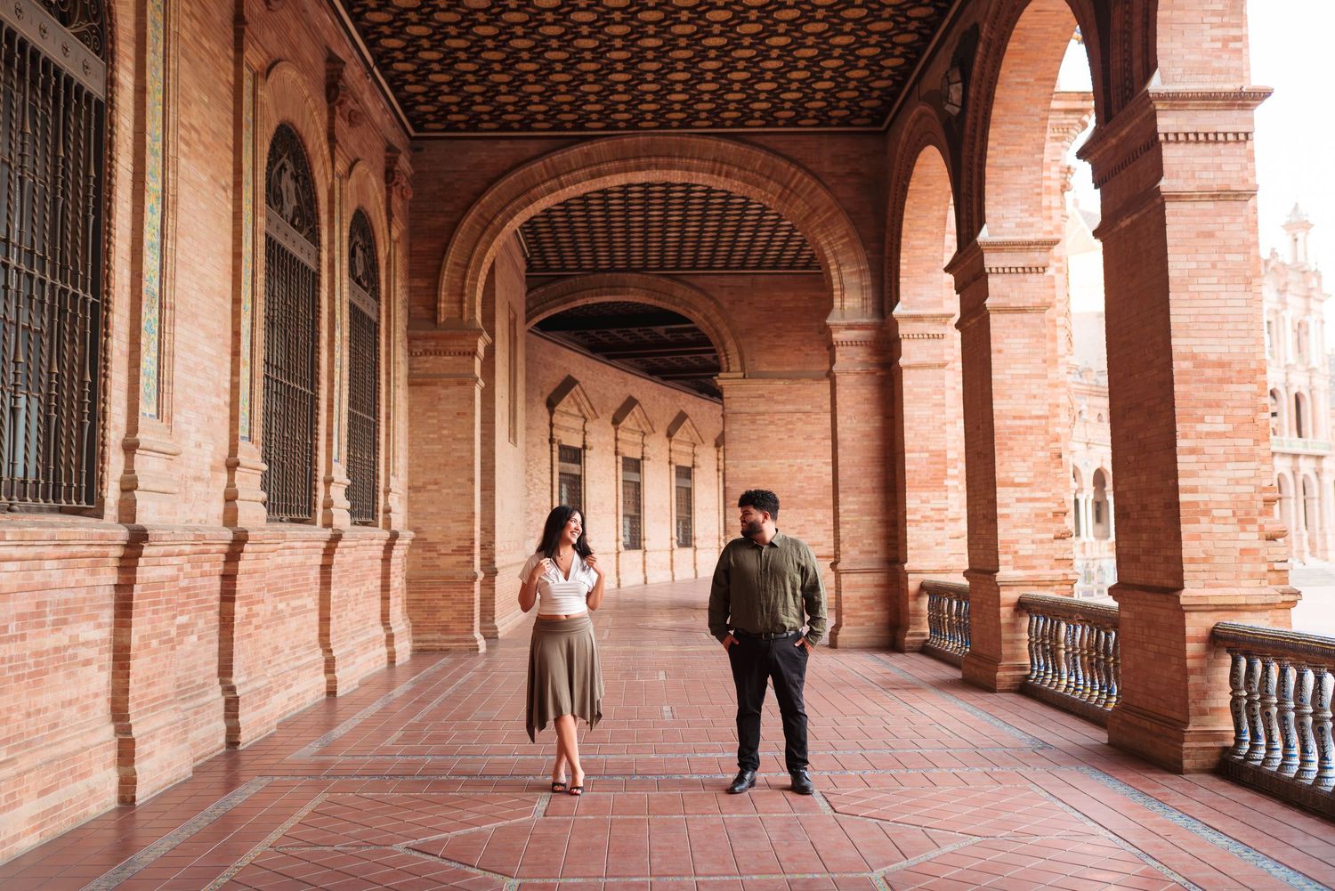 Couple standing in ornate brick archway corridor of Plaza de España, Seville, Spain.