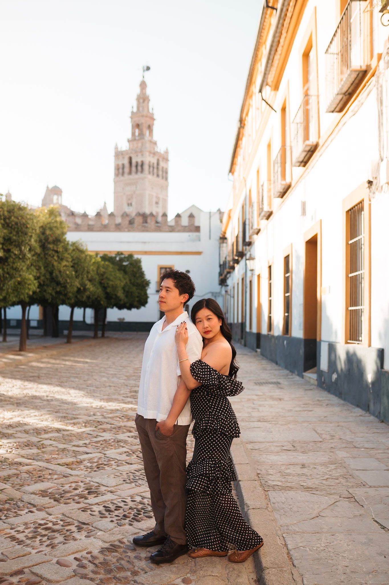 Couple posing near the iconic Giralda tower at golden hour in Seville, Spain.