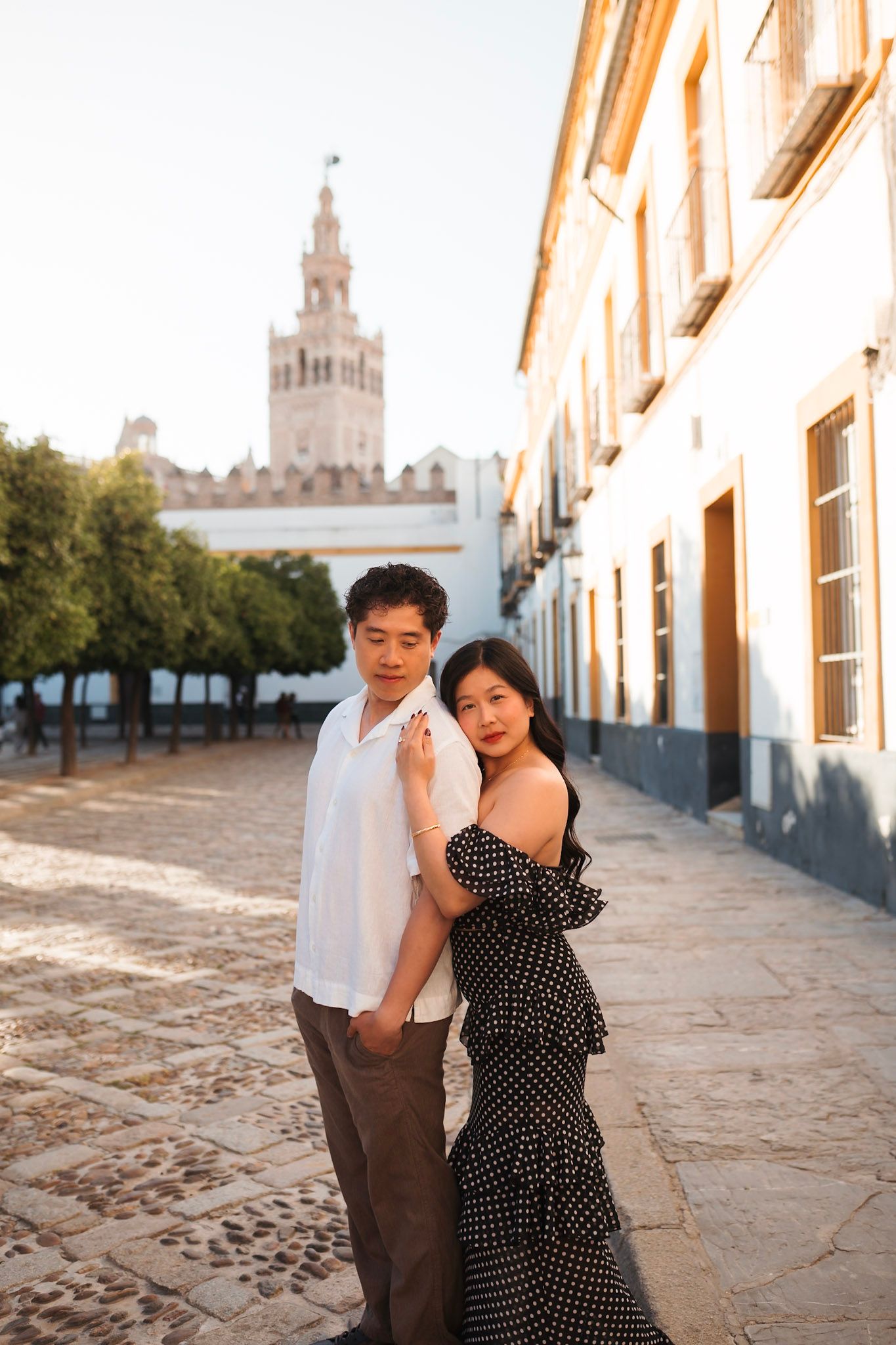 Couple posing romantically on cobblestone street with Giralda tower in Seville, Spain background.