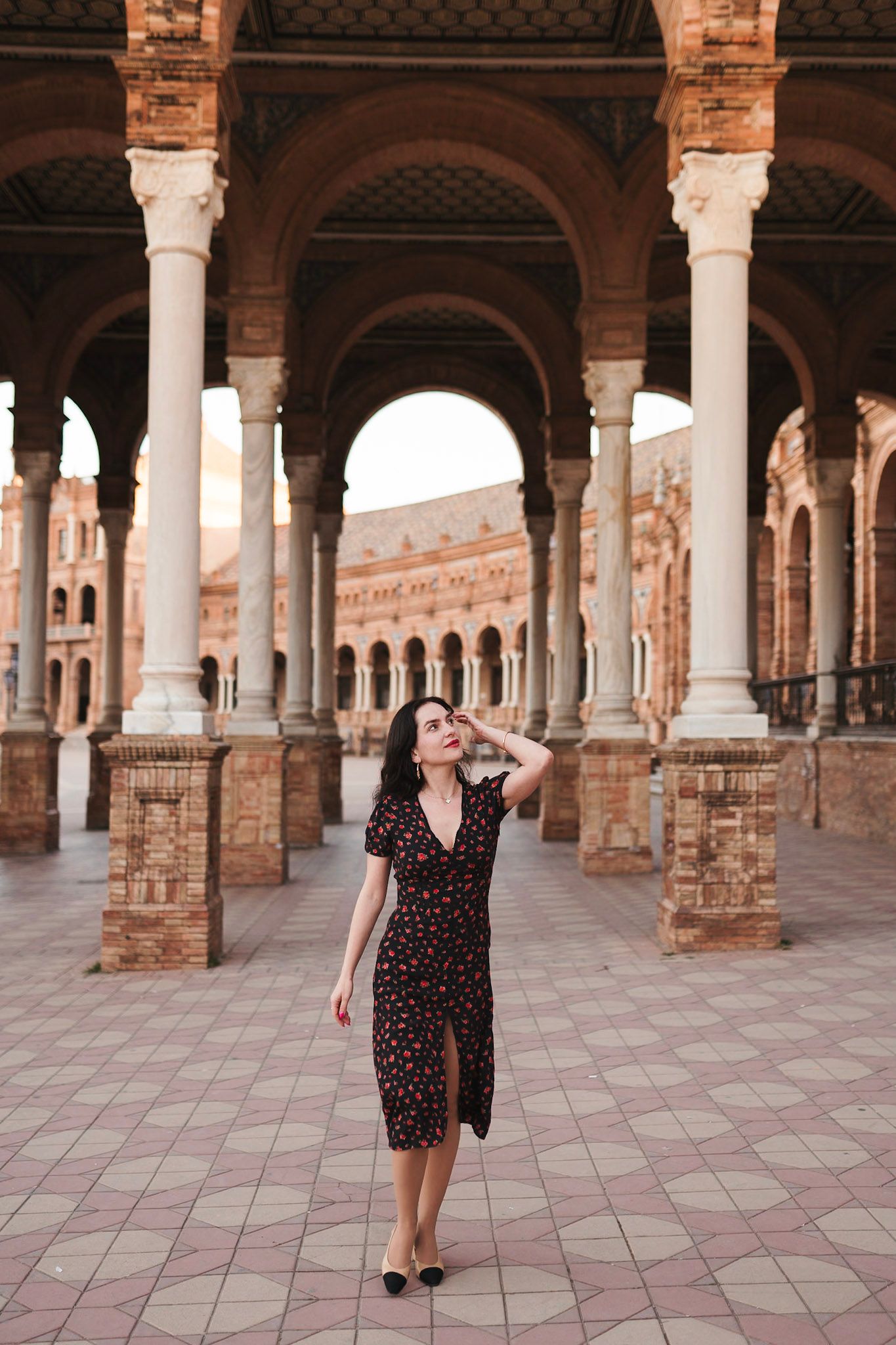 Woman in floral dress posing under arches at Plaza de España, Seville.