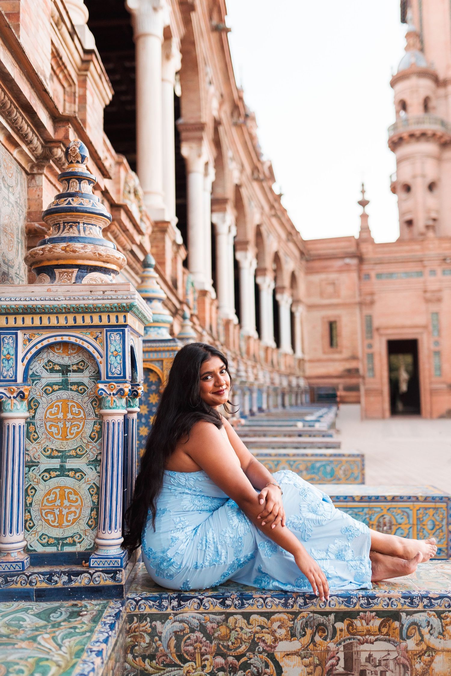 Woman in blue dress sitting on ornate tiled bench at Plaza de España, Seville, Spain.