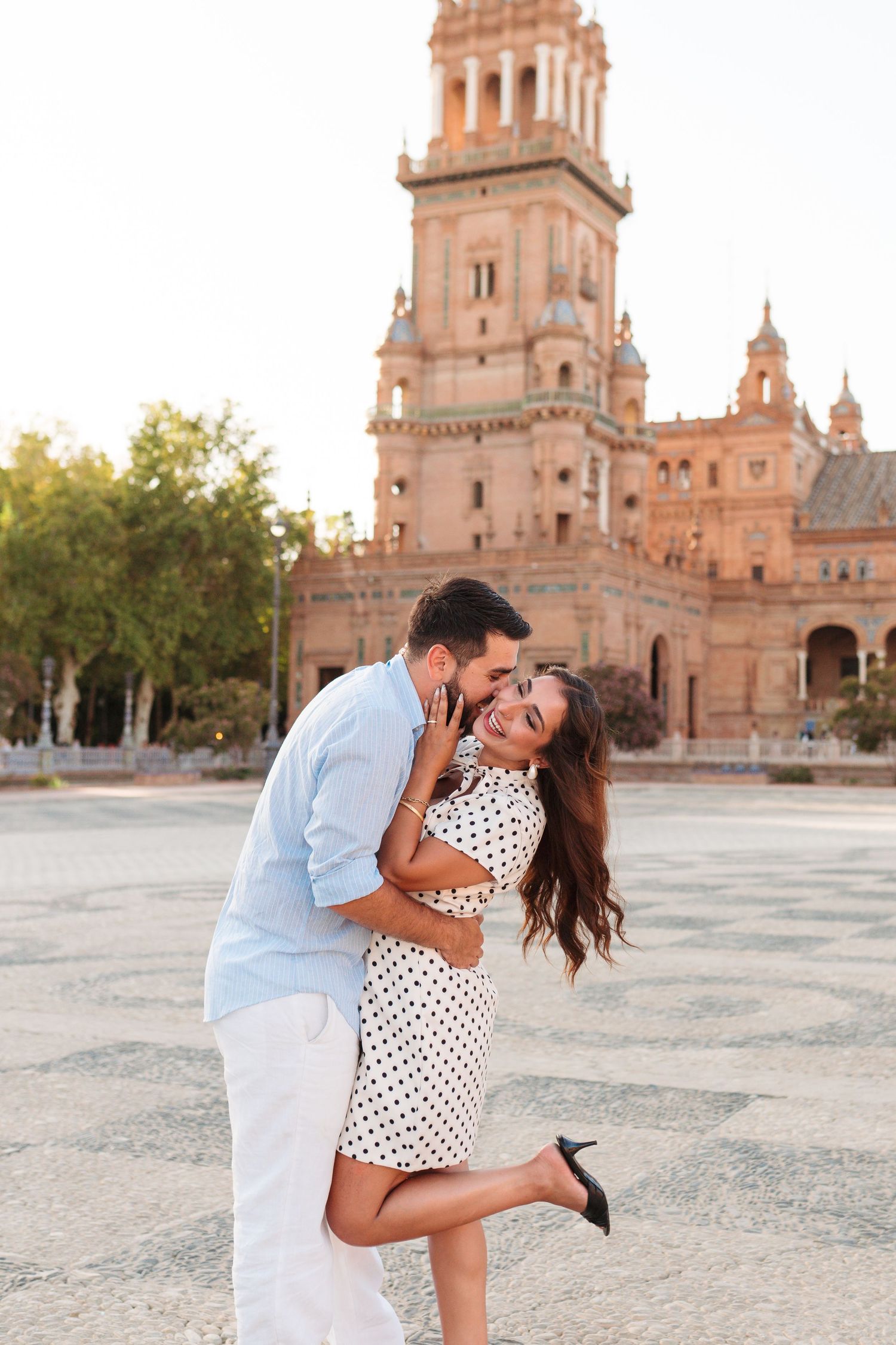 Romantic couple embracing and kissing at Plaza de España, Seville, woman in polka dot dress laughing joyfully.