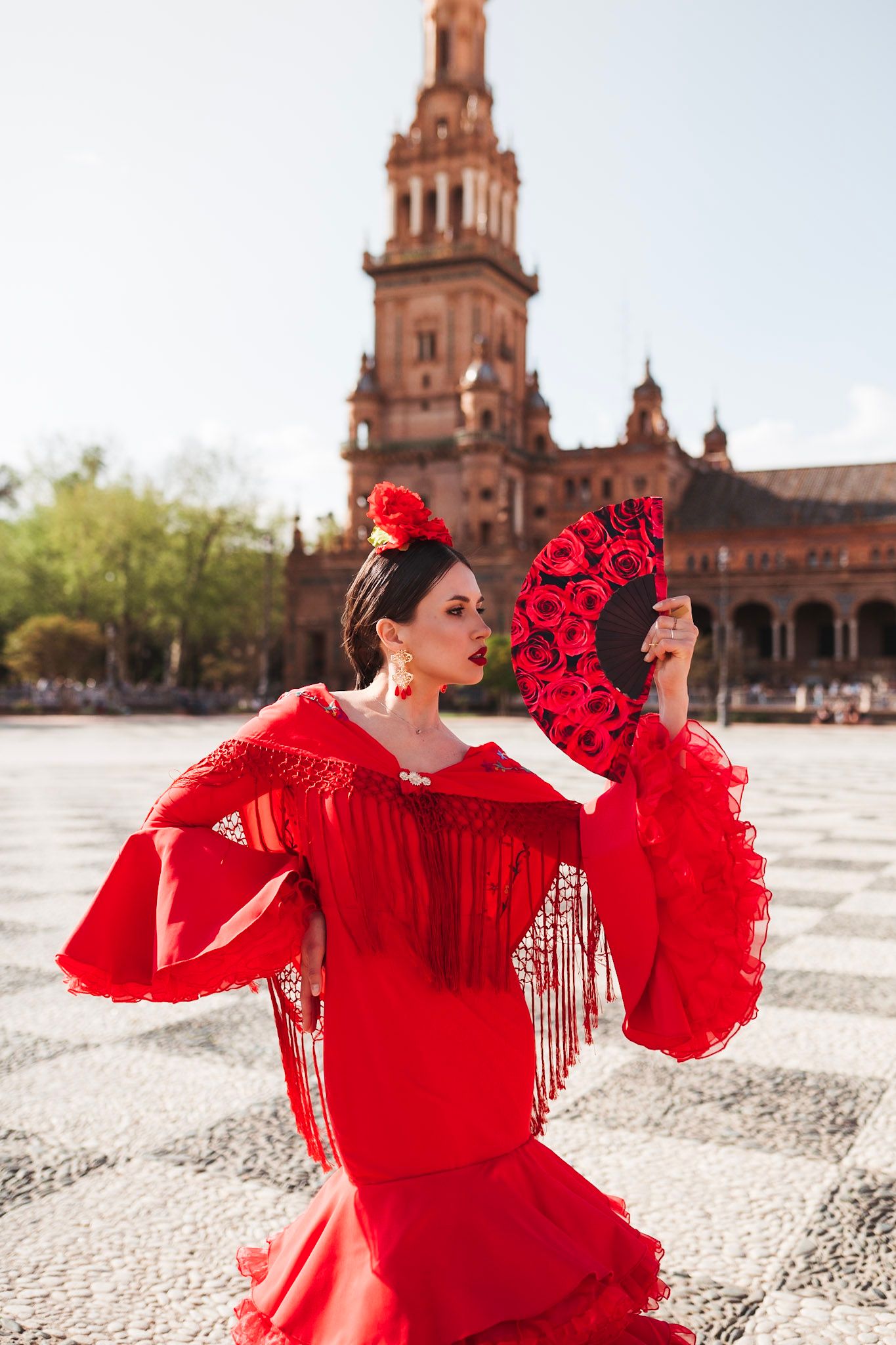 Woman in red flamenco dress holding decorative fan at Plaza de Espana, Seville, Spain.