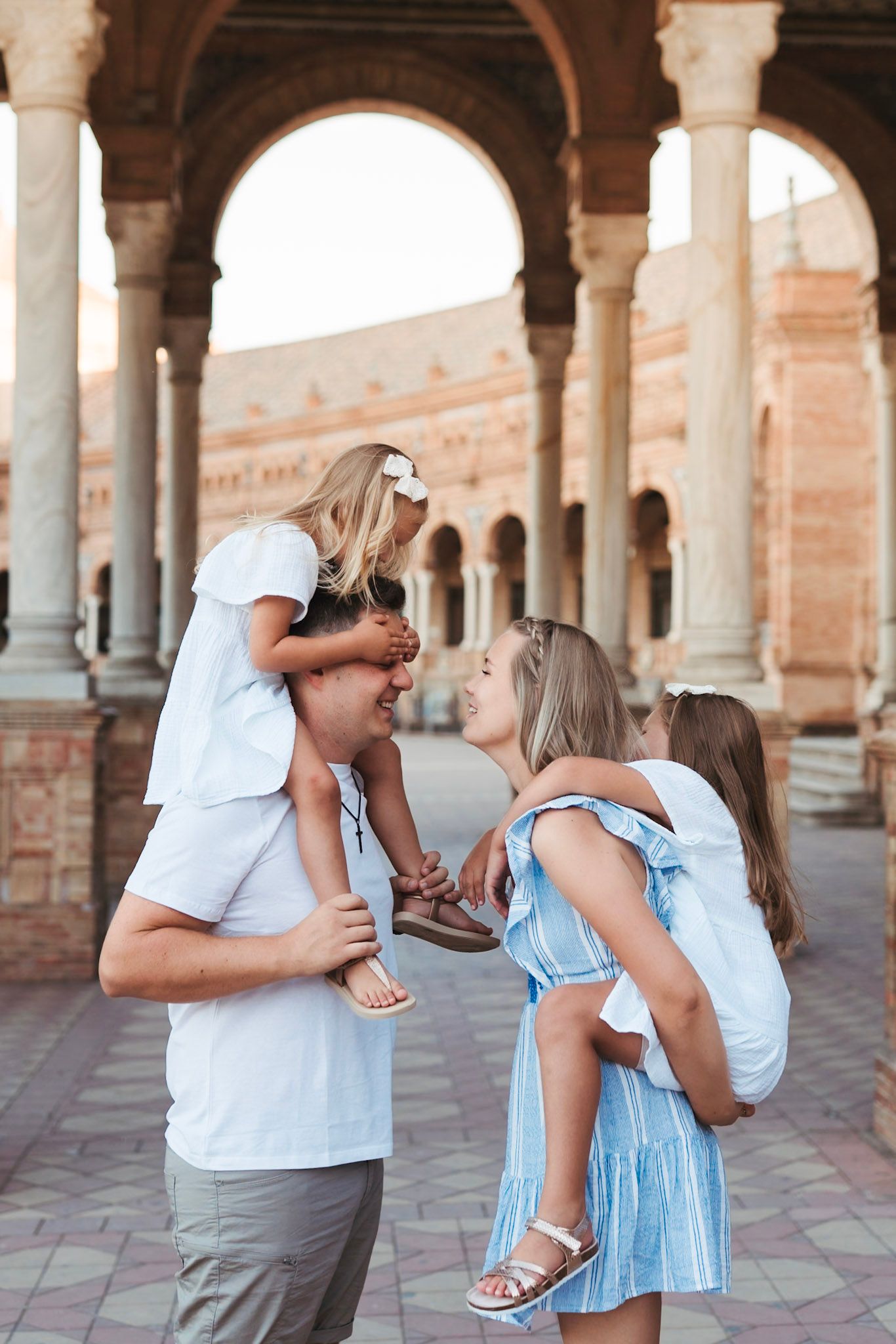 Family with two daughters on shoulders playing at Plaza de España arches in Seville.