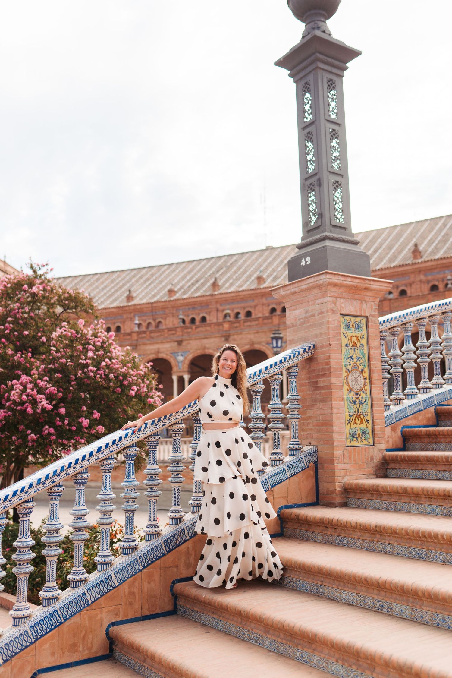 Elegant woman in polka dot outfit posing on tiled steps at Plaza de España, Seville.