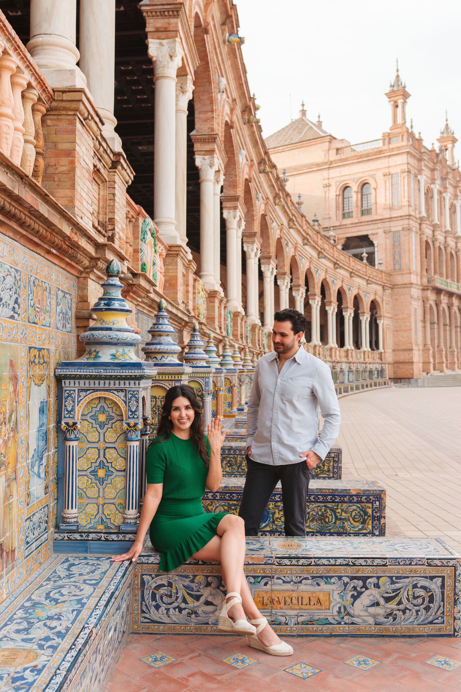 Couple posing at Plaza de España in Seville, Spain, with colorful tiled benches and arched colonnade.