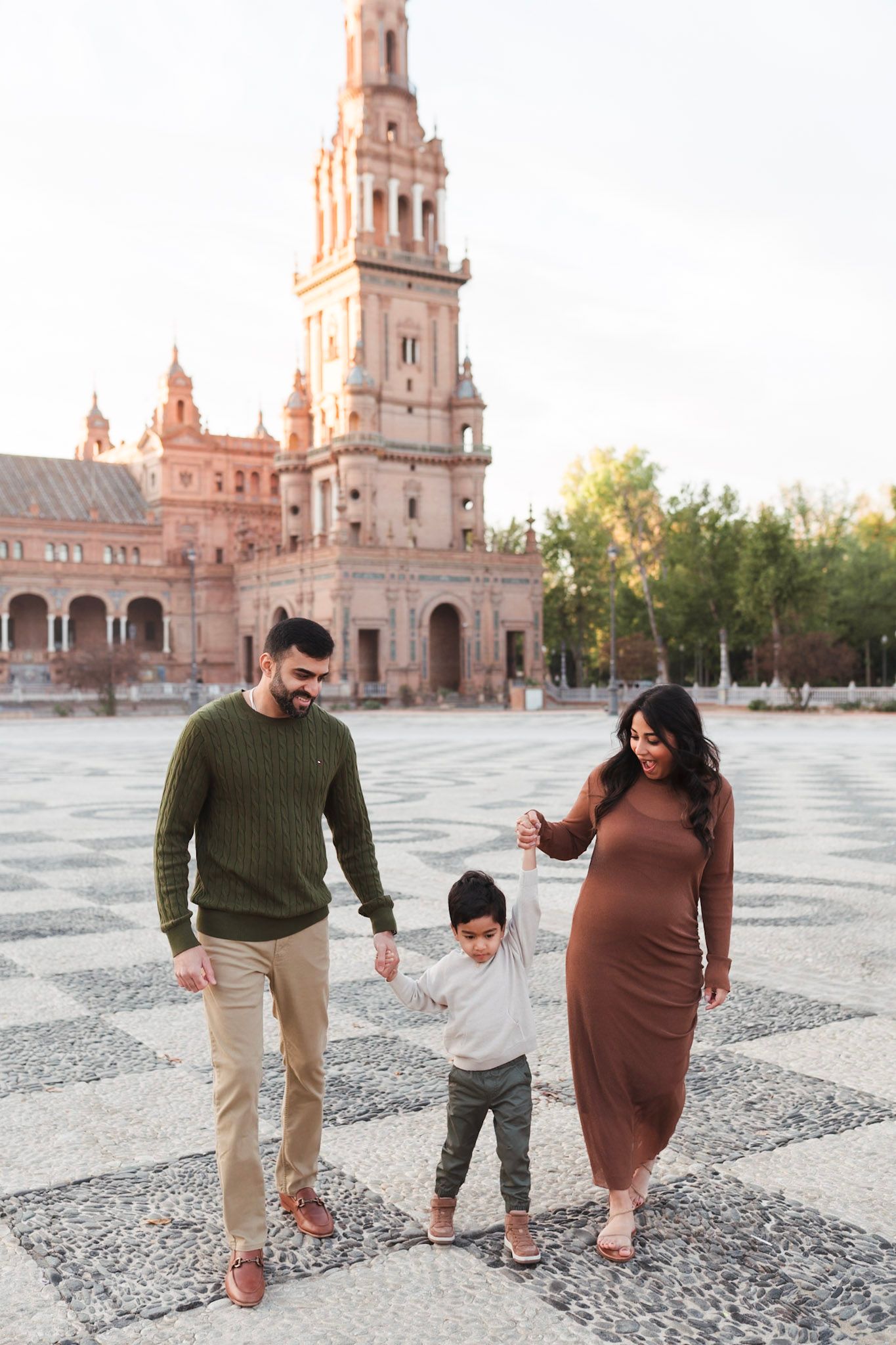 Happy family with toddler and pregnant mother walking at Plaza de España, Seville.