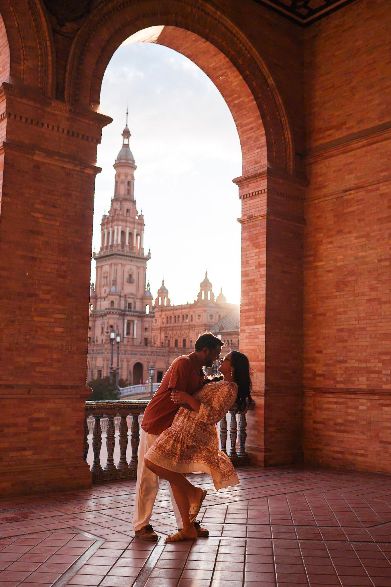 Couple sharing romantic dip kiss under brick arch at Plaza de Espana, Seville, Spain.