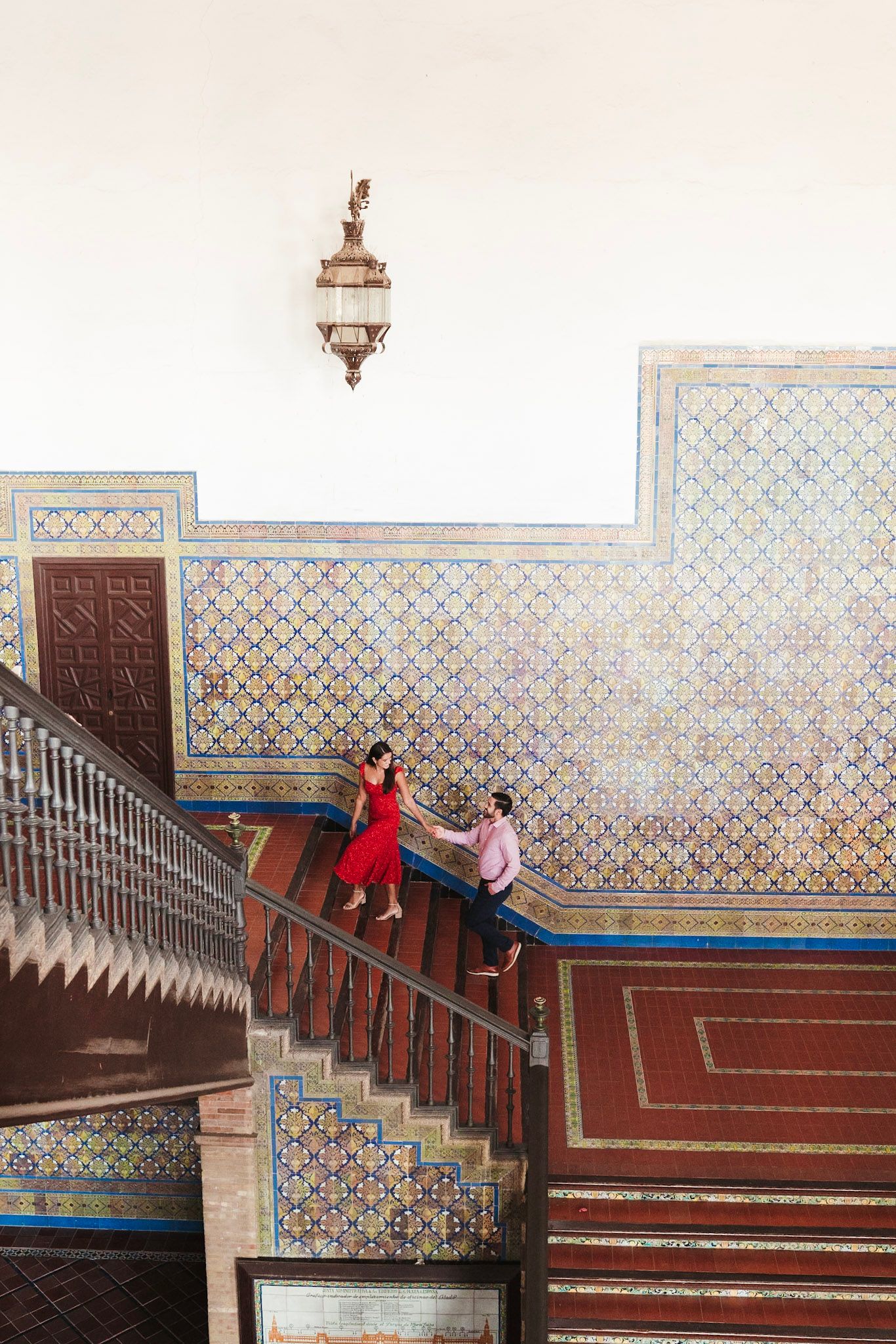 Couple dancing on ornate tiled staircase inside Plaza de España, Seville, with colorful mosaic walls.