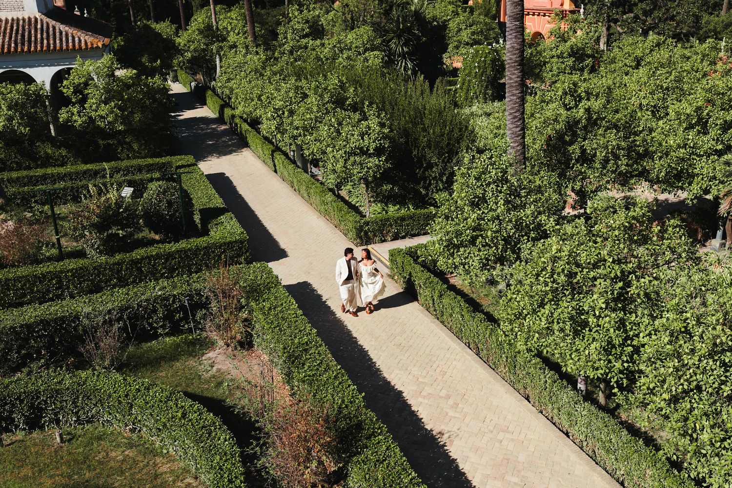 Aerial view of couple walking through lush green hedge maze garden in Seville, Spain.