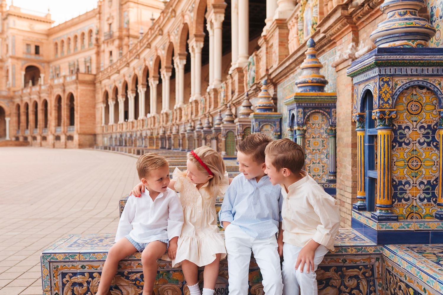Four young children sitting and chatting on ornate tiled bench at Plaza de Espana, Seville.