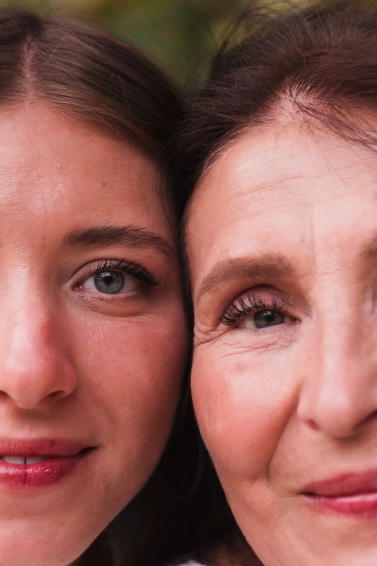 Close-up portrait of young woman and older woman cheek to cheek, showing generational bond.