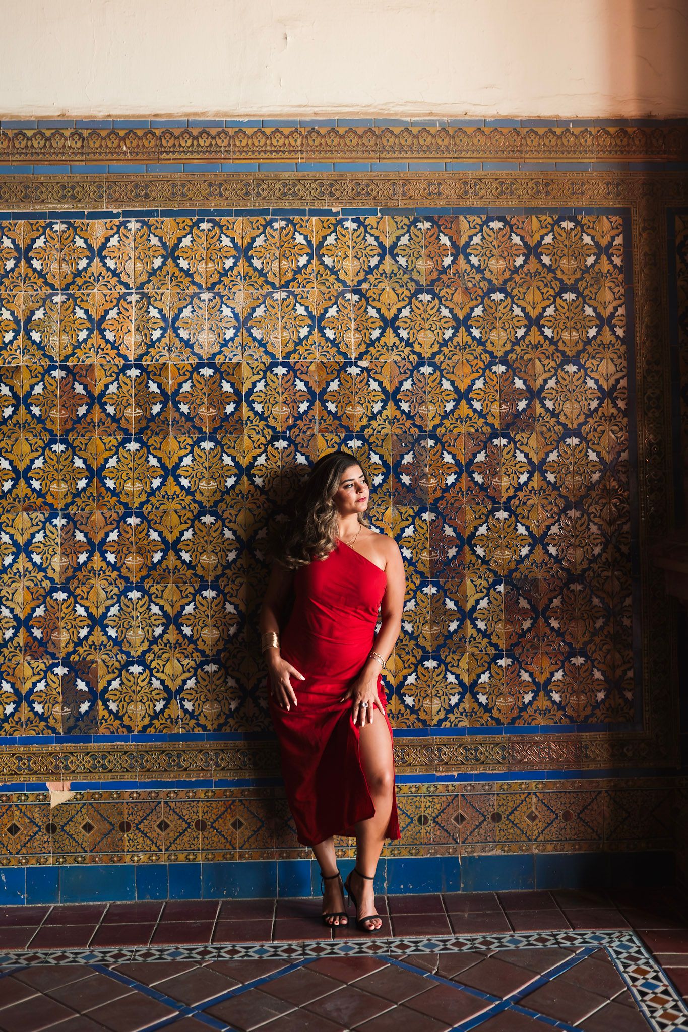Woman in red dress poses against ornate blue and gold mosaic tile wall.