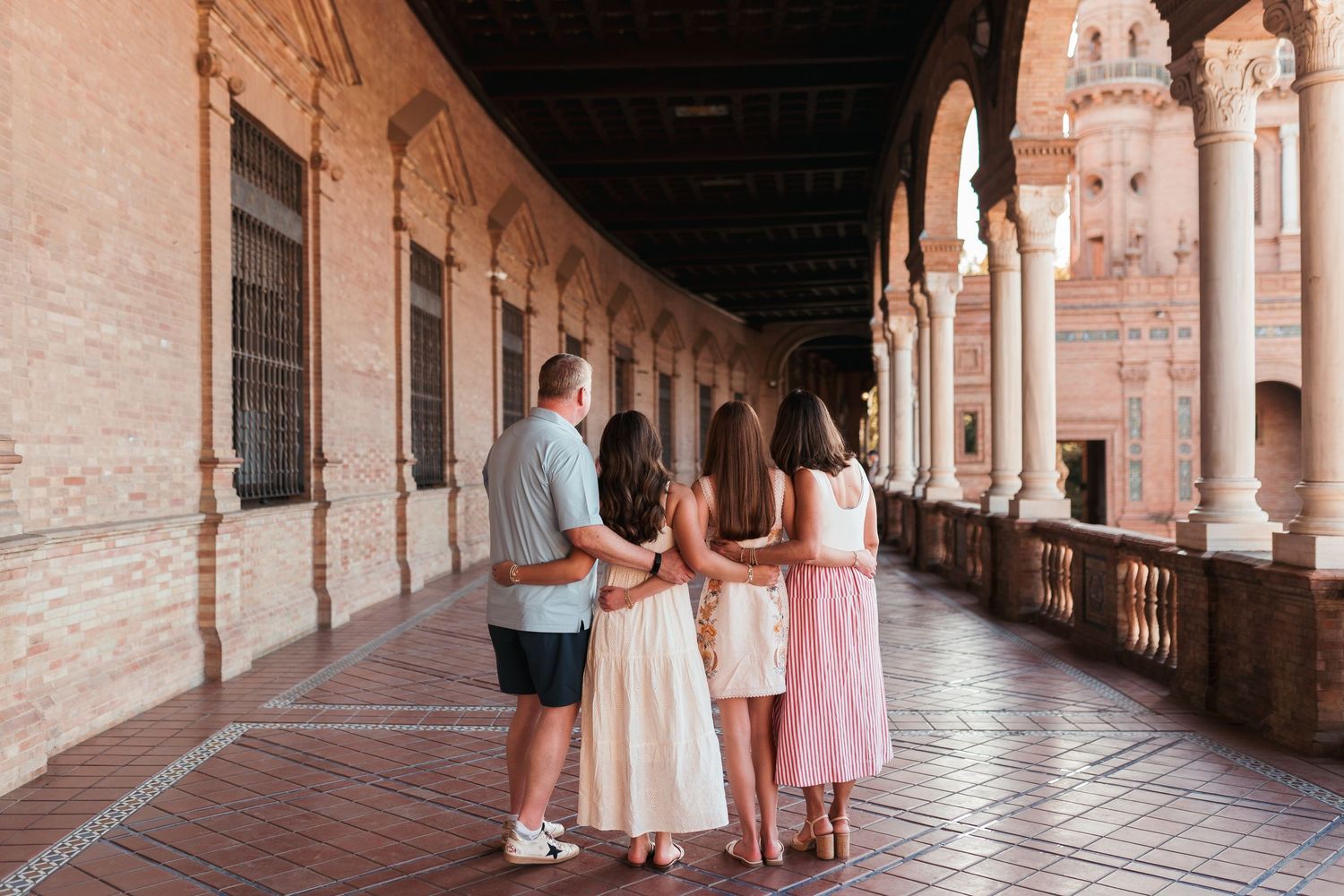 Family of three standing together in a stunning Spanish plaza arcade, admiring the ornate architecture and arched columns.