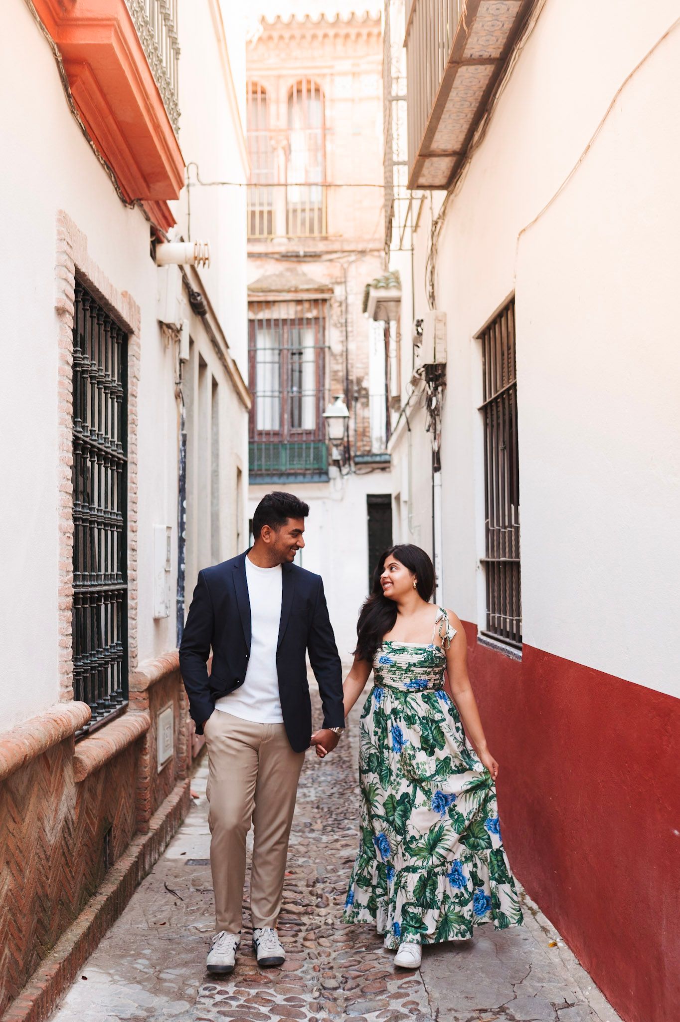 Couple holding hands and walking through a narrow cobblestone alley in Seville, Spain.