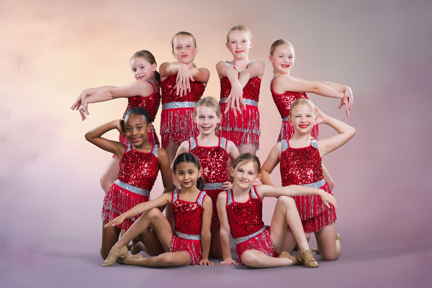 Nine young dancers in red sequin costumes pose together for a studio group portrait.