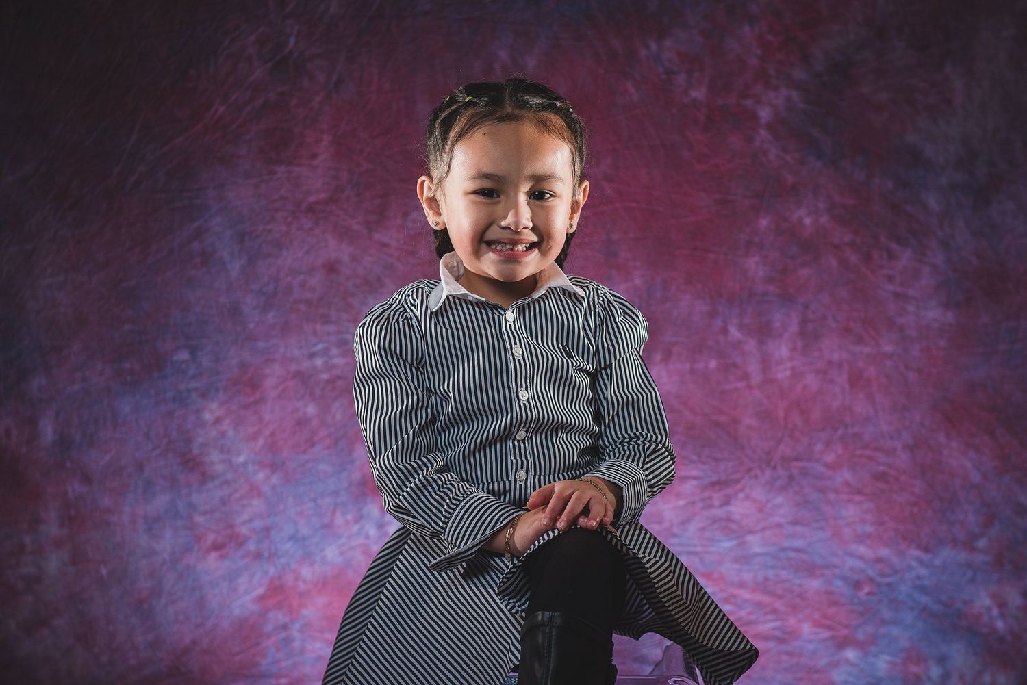 Adorable young girl in striped dress smiling and posing for a studio portrait photo.