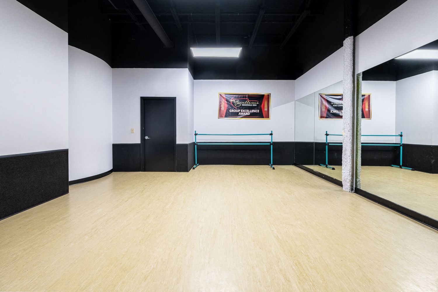 Bright dance studio with hardwood floors, ballet barres, wall mirrors, and a red banner in a spacious black and white room.