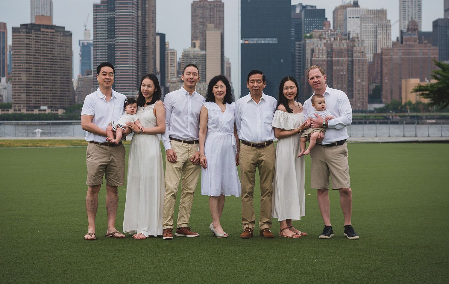 Family portrait of seven people posing on a green lawn with NYC skyline in background.